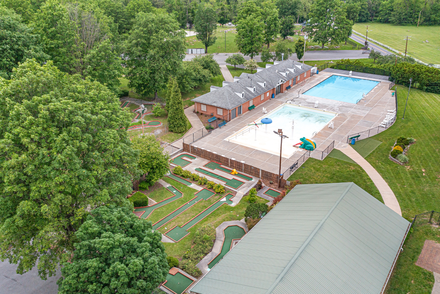 Aerial view of a recreational area featuring a swimming pool, splash pad, and mini-golf course surrounded by lush greenery.