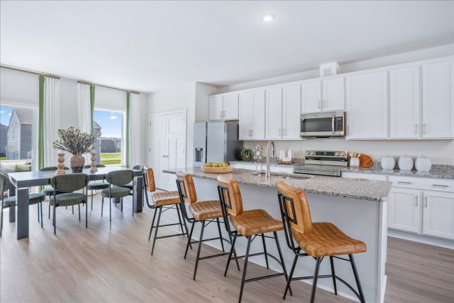 Modern open-concept kitchen and dining area with white cabinets, granite countertops, and stylish bar stools.