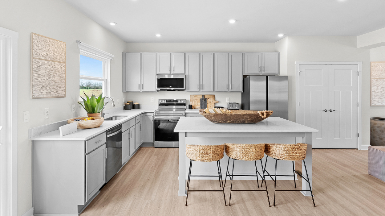 Modern white kitchen with stainless steel appliances, island seating, and light wood flooring.