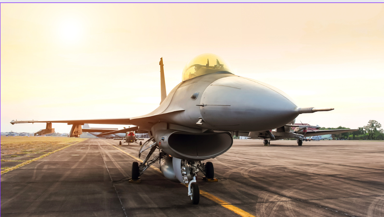 A sleek military jet parked on an airstrip under a bright sunrise sky.