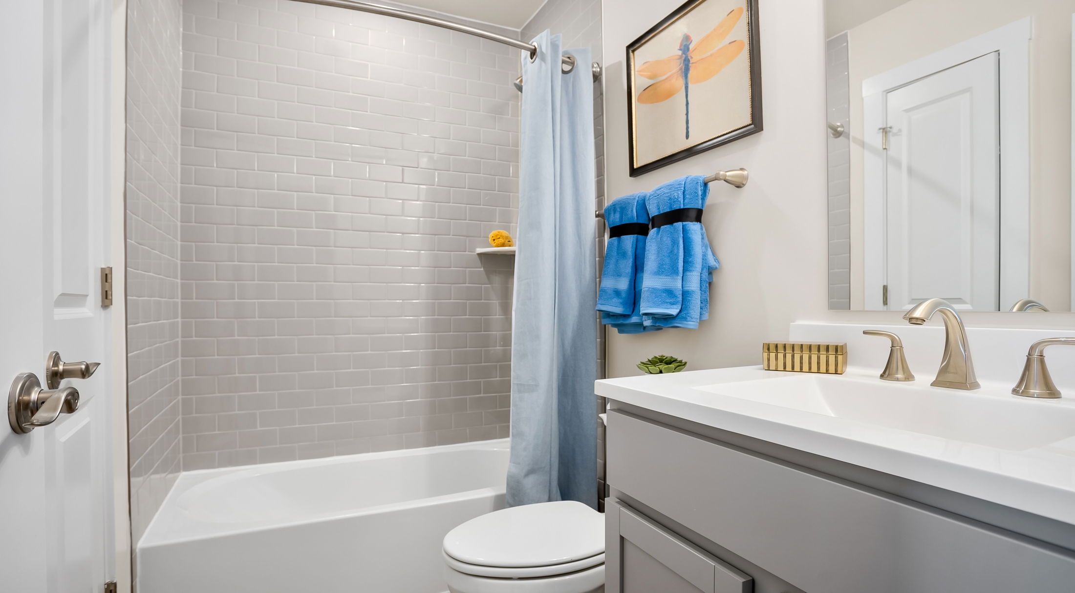 Modern bathroom with gray subway tiles, a white bathtub, and blue towels.