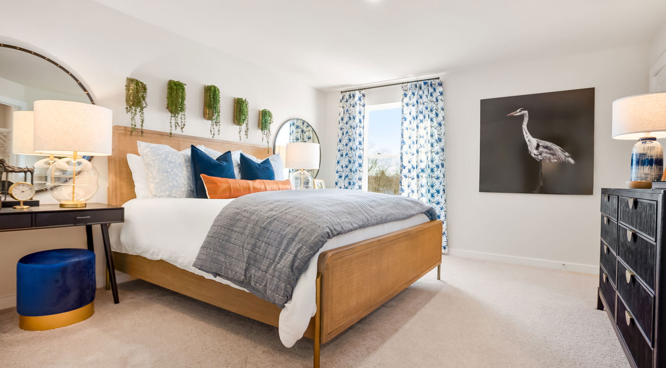 Modern bedroom with a wooden bed, blue and white decor accents, large windows, and nature-inspired art.