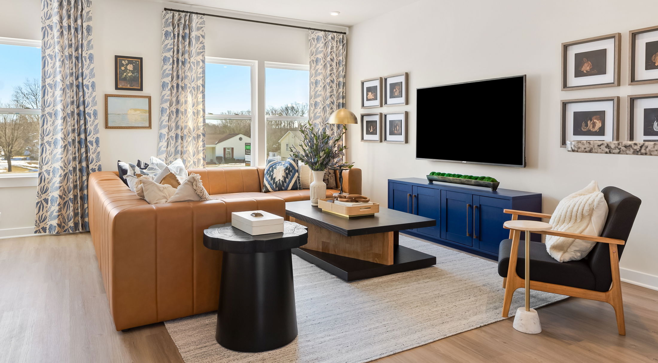 Contemporary living room with a brown leather sectional, modern furniture, and a large flat-screen TV on a white wall.