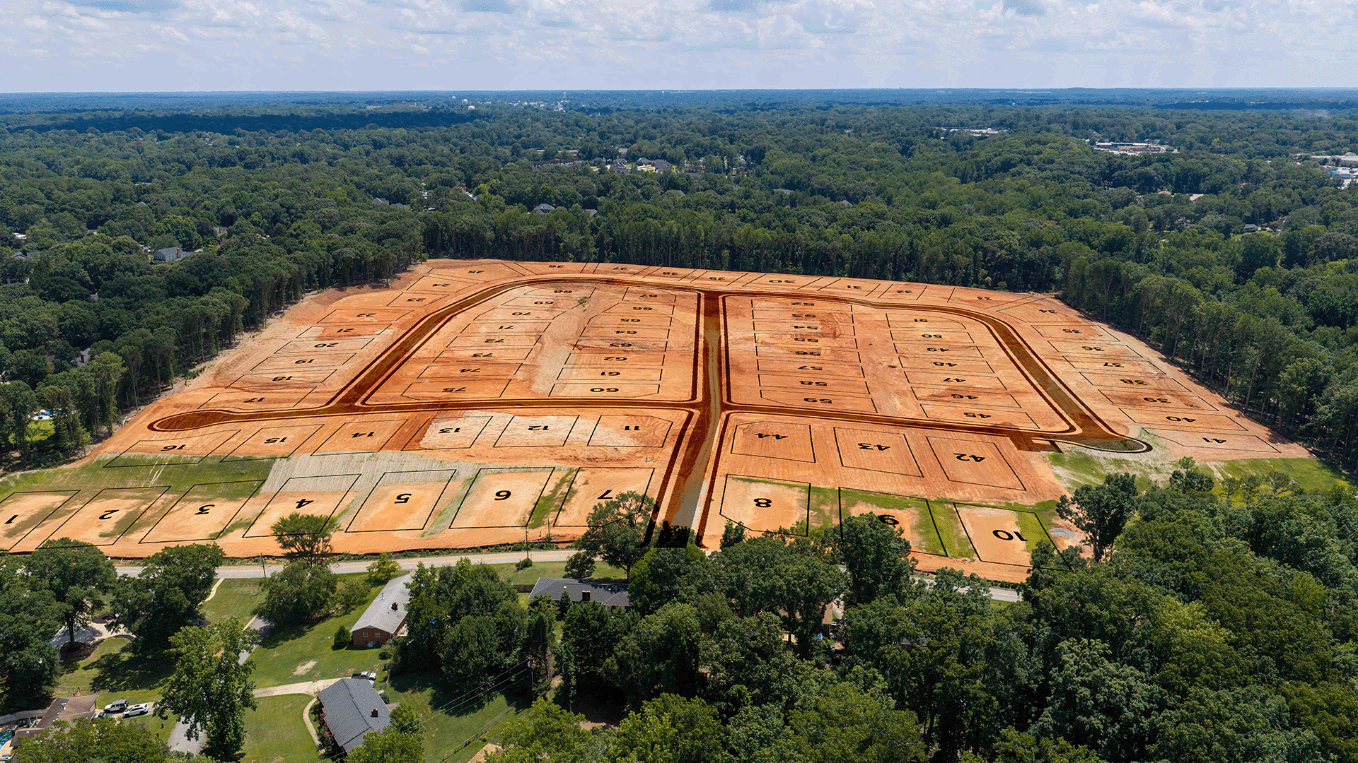 Aerial view of a cleared land plot with numbered sections for residential development, surrounded by trees and existing homes.