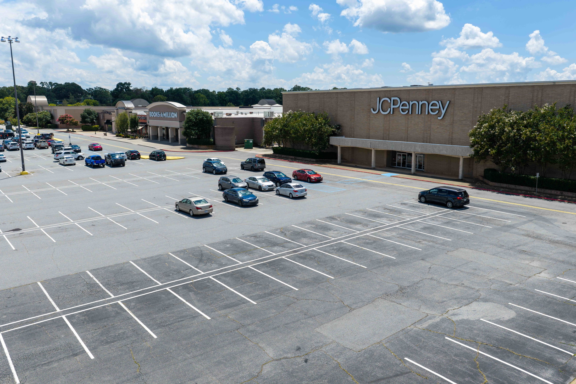 A nearly empty parking lot outside a JCPenney store, with a few cars parked and a cloudy sky above.