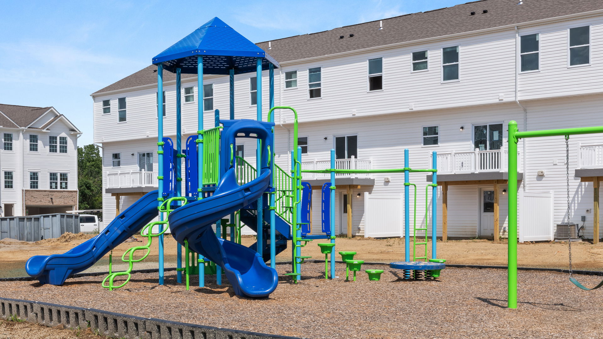 Modern outdoor playground with blue and green slides and swings located in a residential neighborhood.