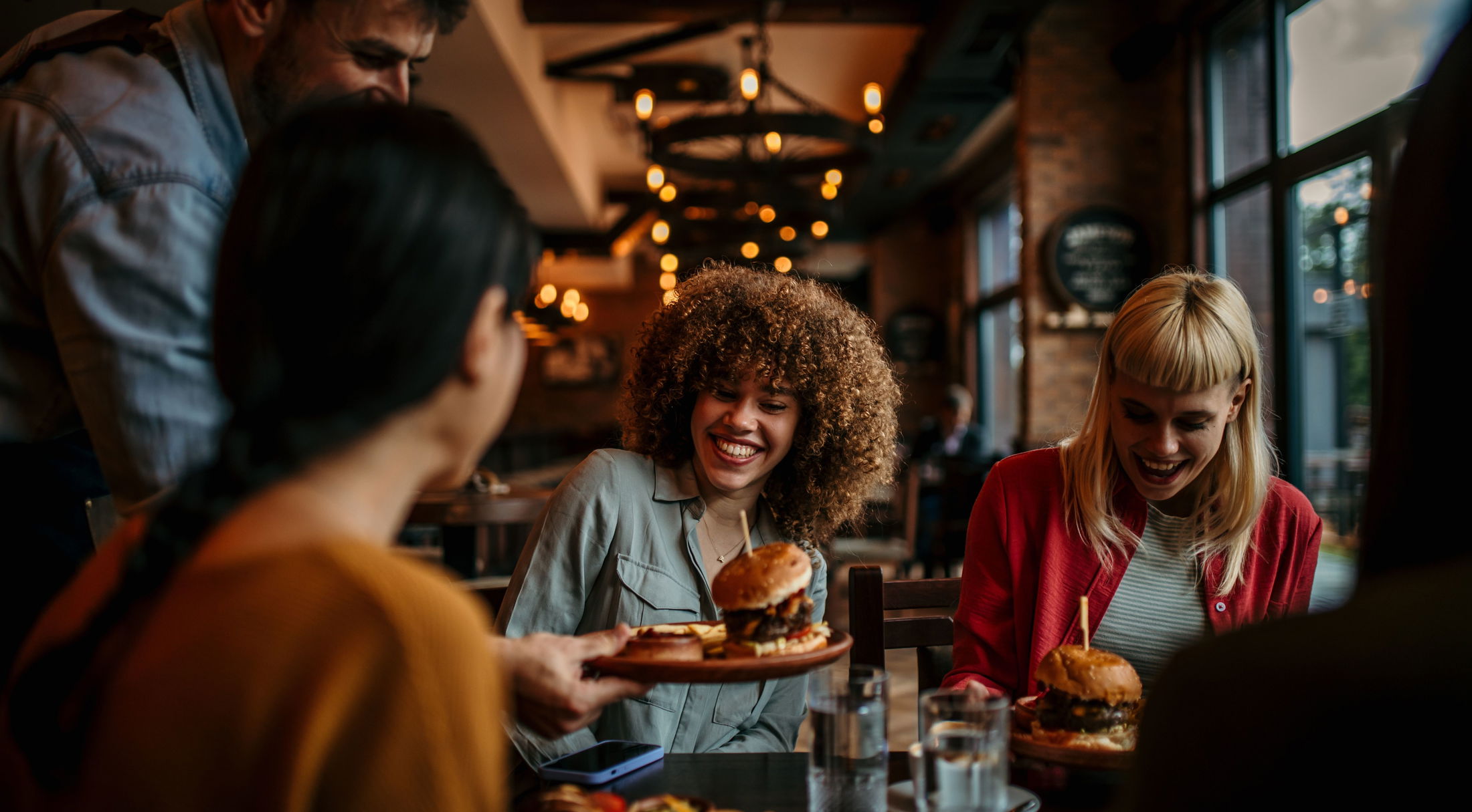 Group of friends enjoying burgers at a cozy restaurant with warm lighting.