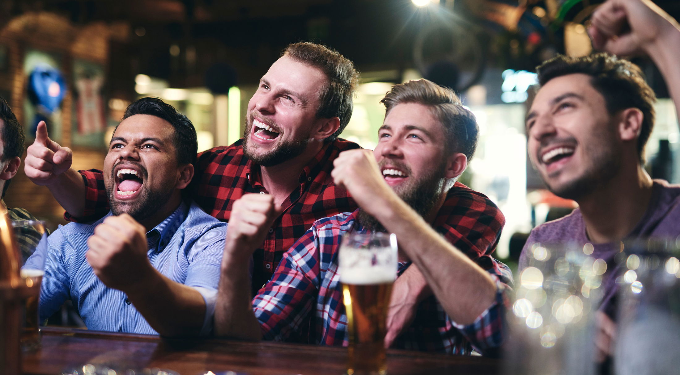 A group of enthusiastic friends cheering together in a lively bar setting.