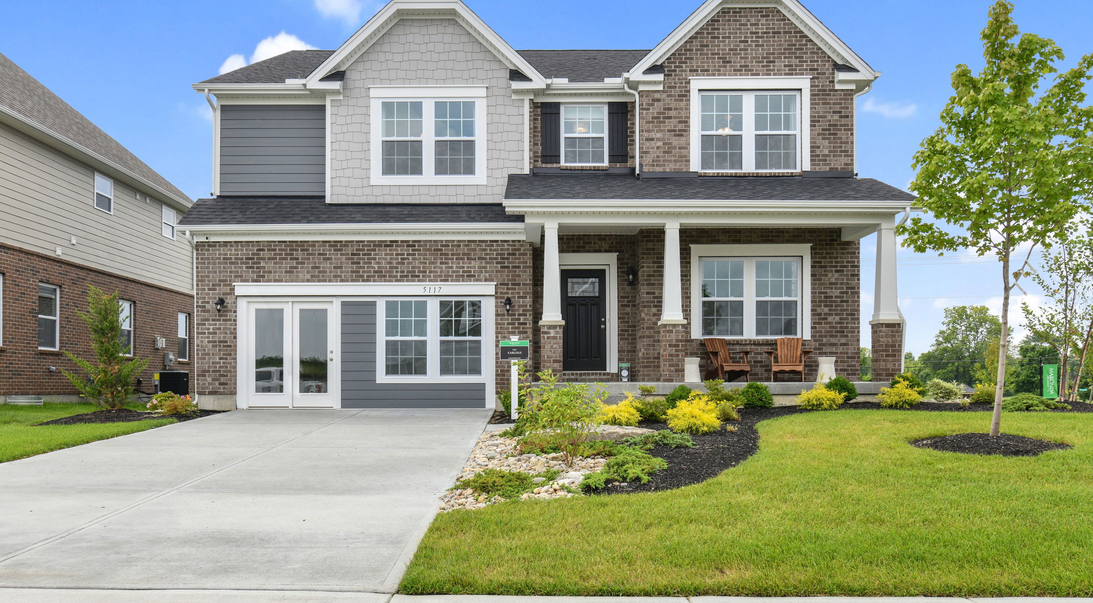 Modern two-story brick house with a manicured lawn and large driveway under a clear blue sky.