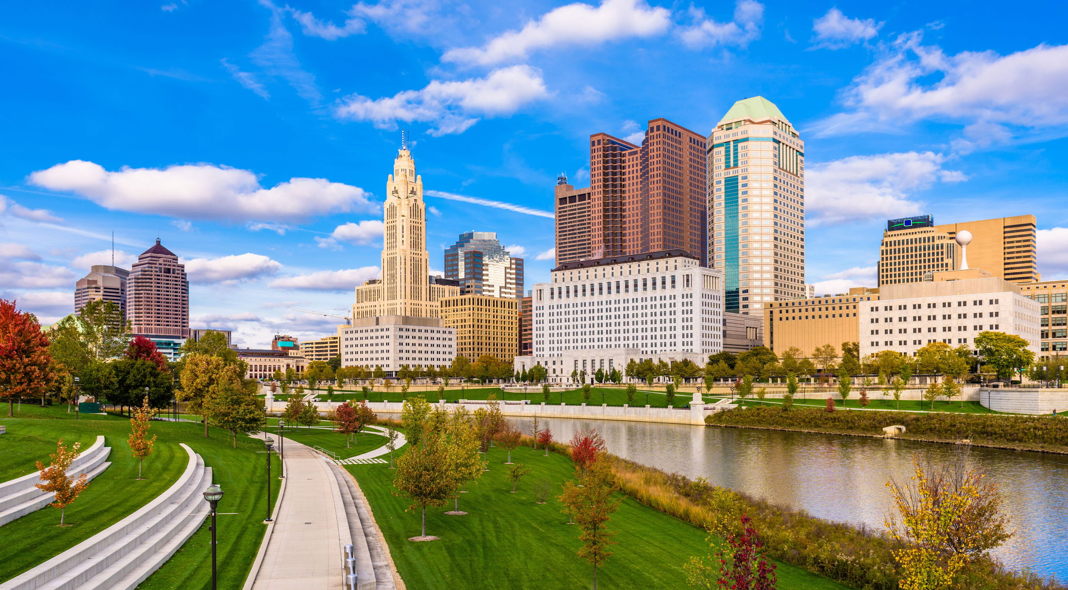 Skyline of Columbus, Ohio with modern skyscrapers, green park, and river under a blue sky.