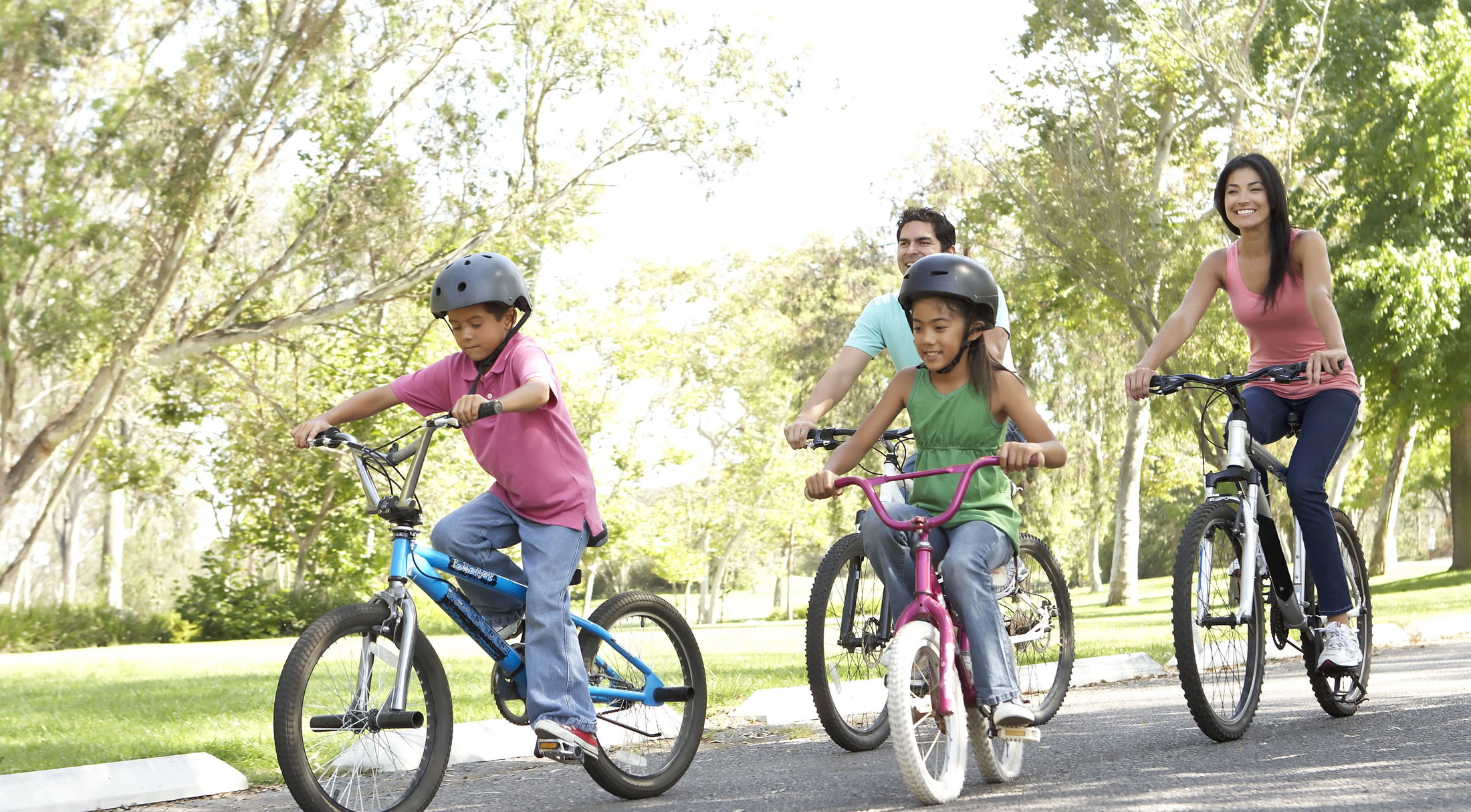 A family enjoying a bike ride together in a sunny park, wearing helmets for safety.