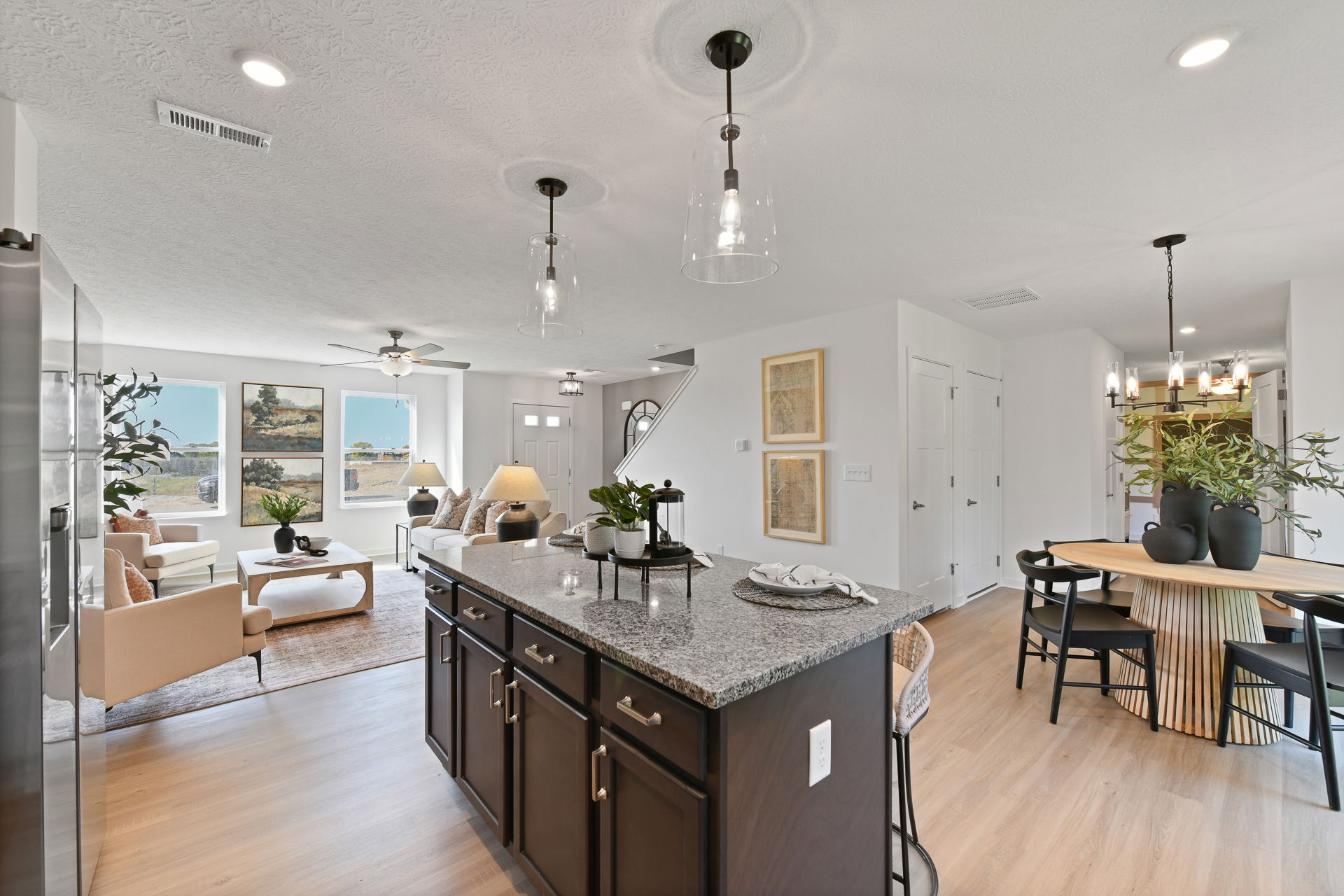 Open-concept living room and kitchen with modern decor, featuring a granite island, wooden dining table, and stylish lighting fixtures.