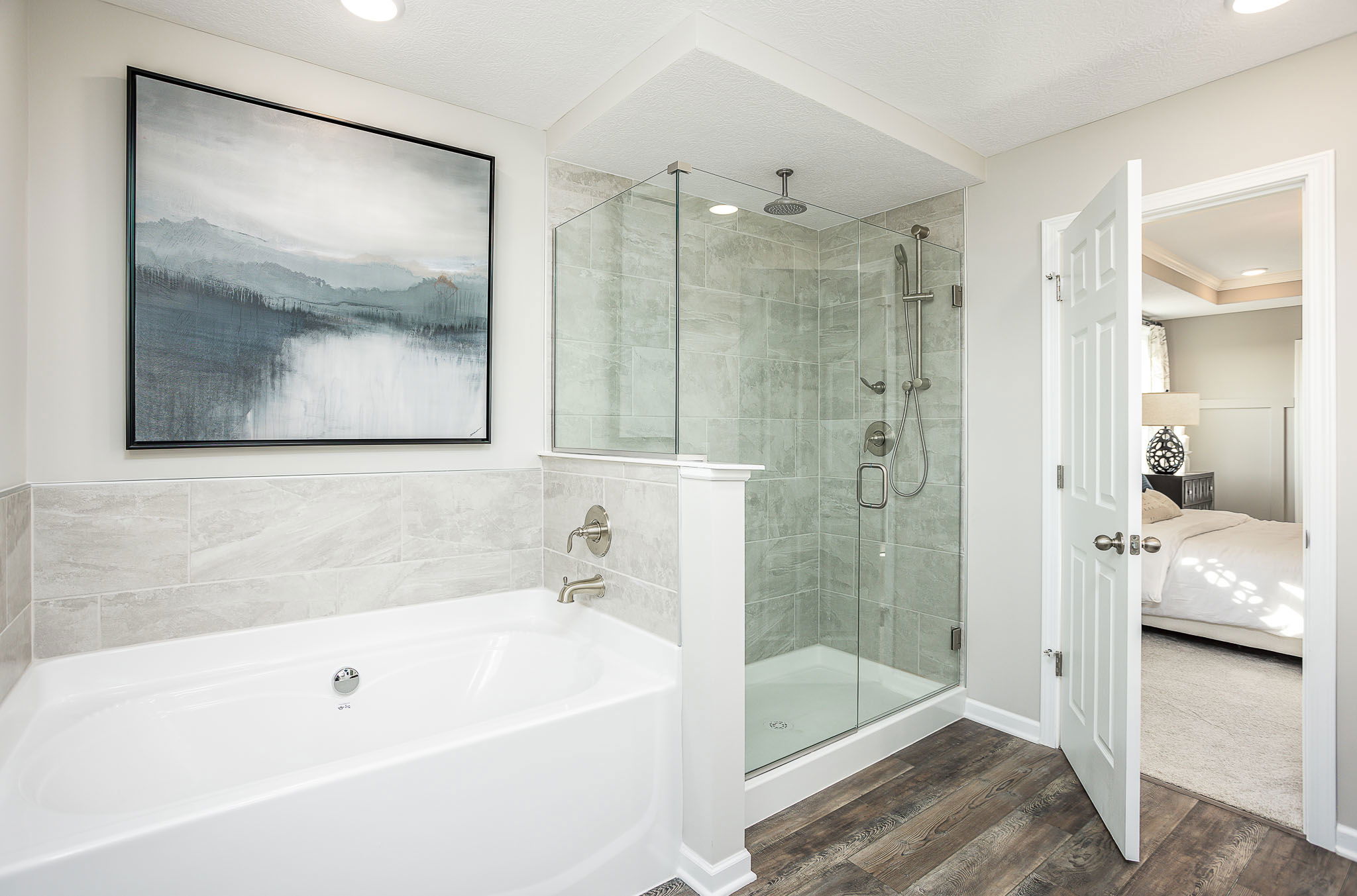 Modern bathroom with glass-enclosed shower, large bathtub, and serene landscape art on the wall.