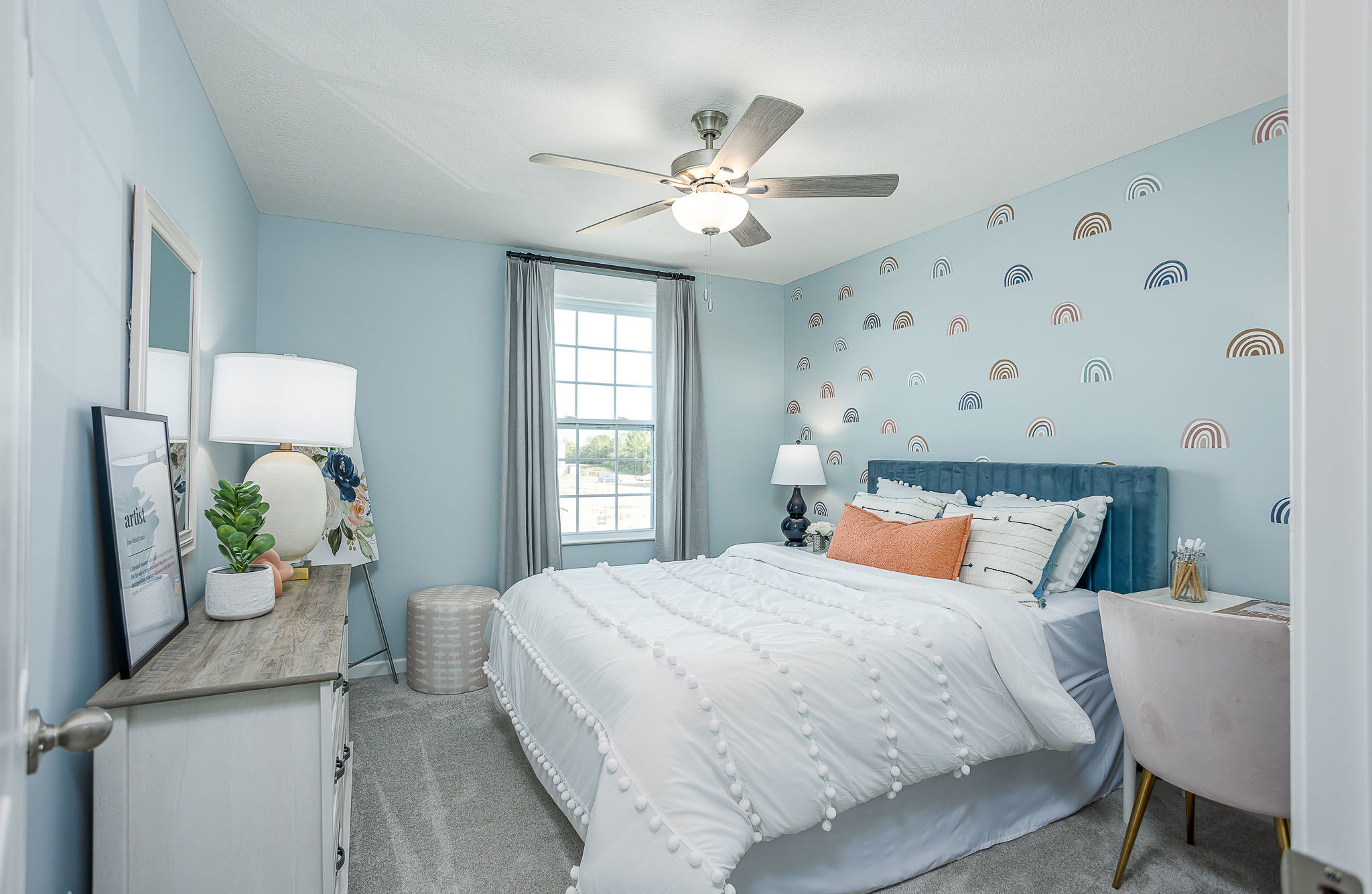 Modern bedroom with light blue walls, a rainbow accent, and cozy decor featuring a plush bed and stylish furniture.