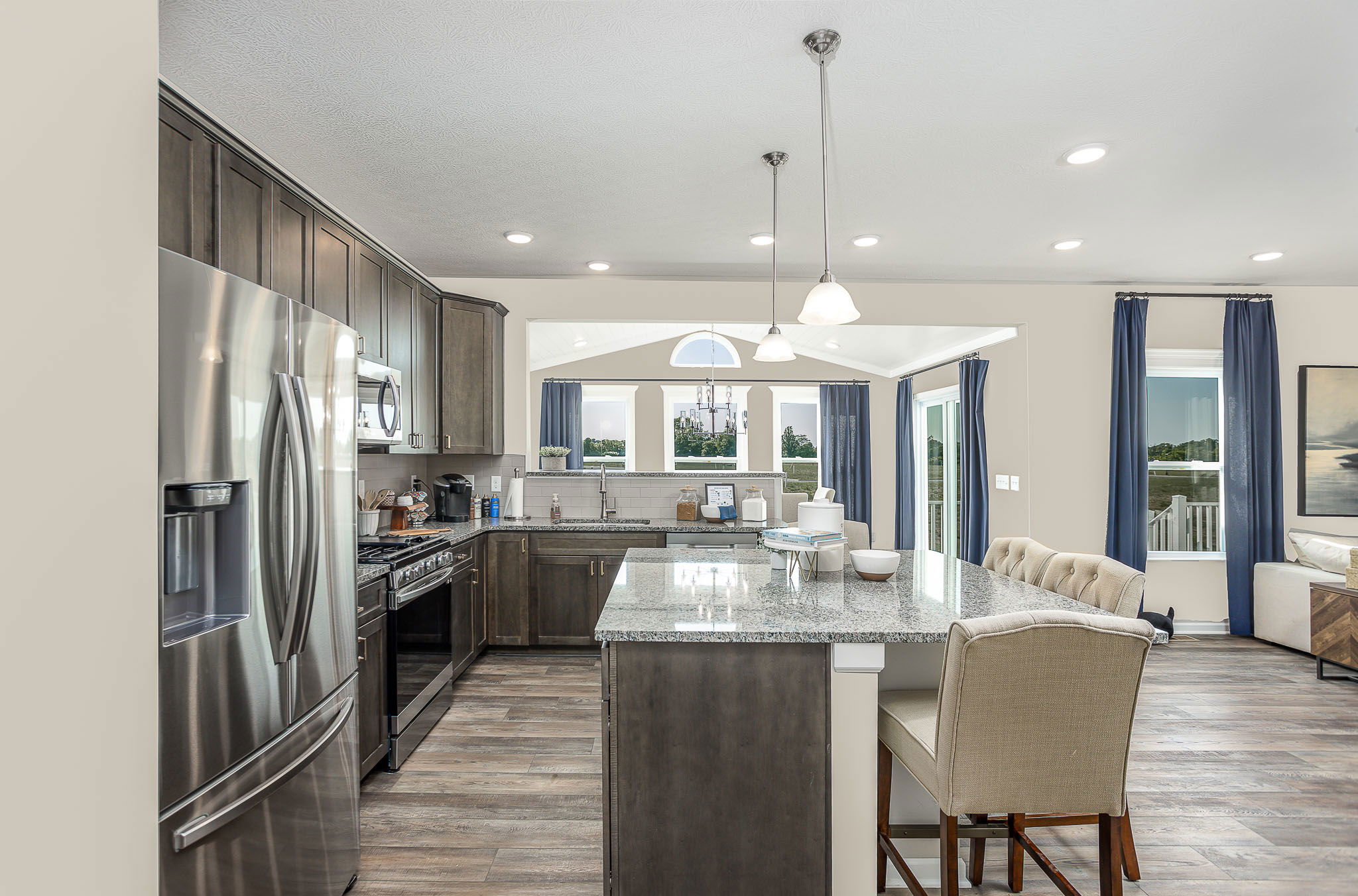 Modern kitchen with stainless steel appliances, granite countertops, dark wood cabinets, and a large island with seating.