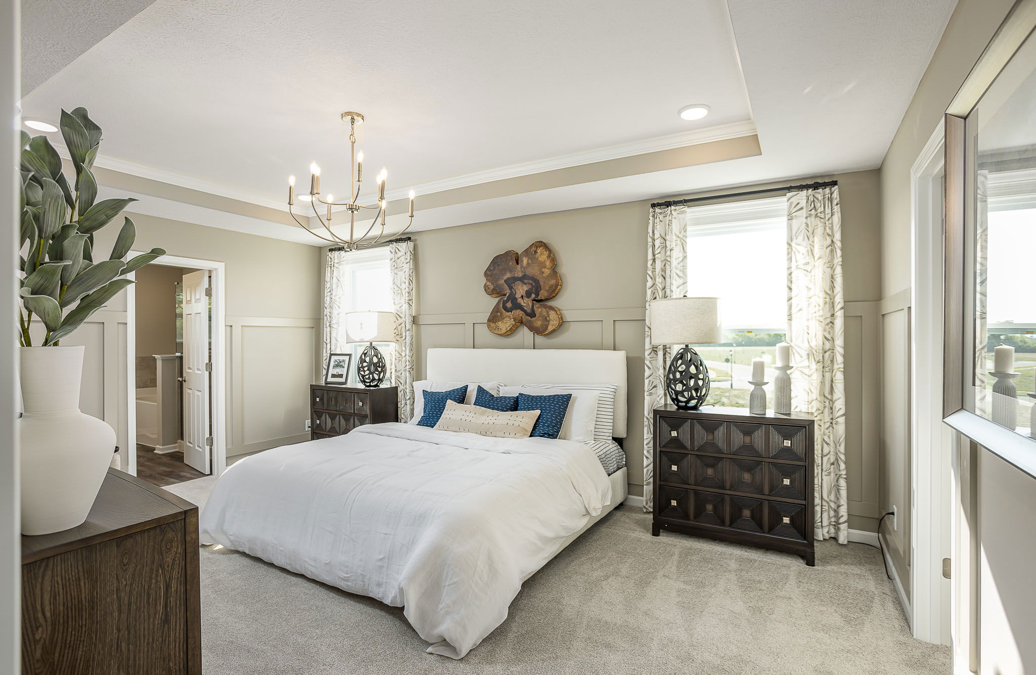 Luxurious modern bedroom with elegant decor, featuring a large bed, wooden furniture, stylish lighting, and green plant accents.