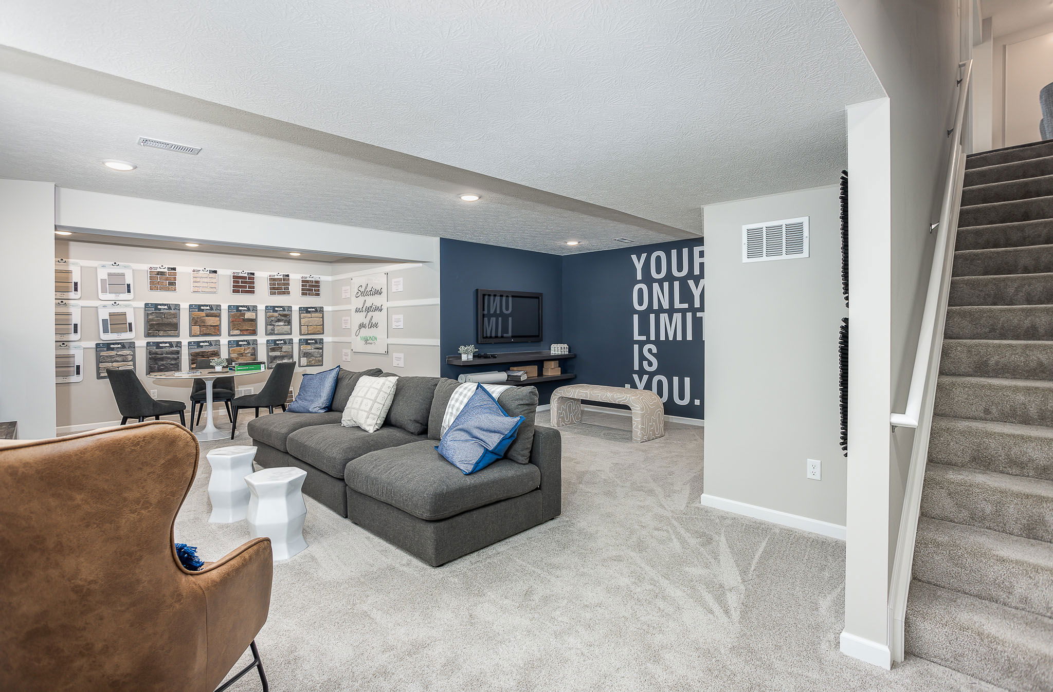 A modern basement living space with gray sectional sofa, motivational wall art, and carpeted floors, creating a cozy and inviting atmosphere.