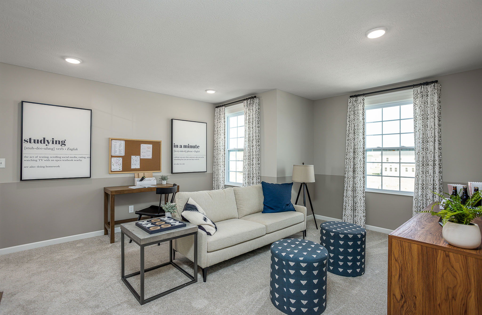 Modern living room with beige sofa, blue cushions, framed wall art, and a wooden desk, featuring a minimalist and cozy design.