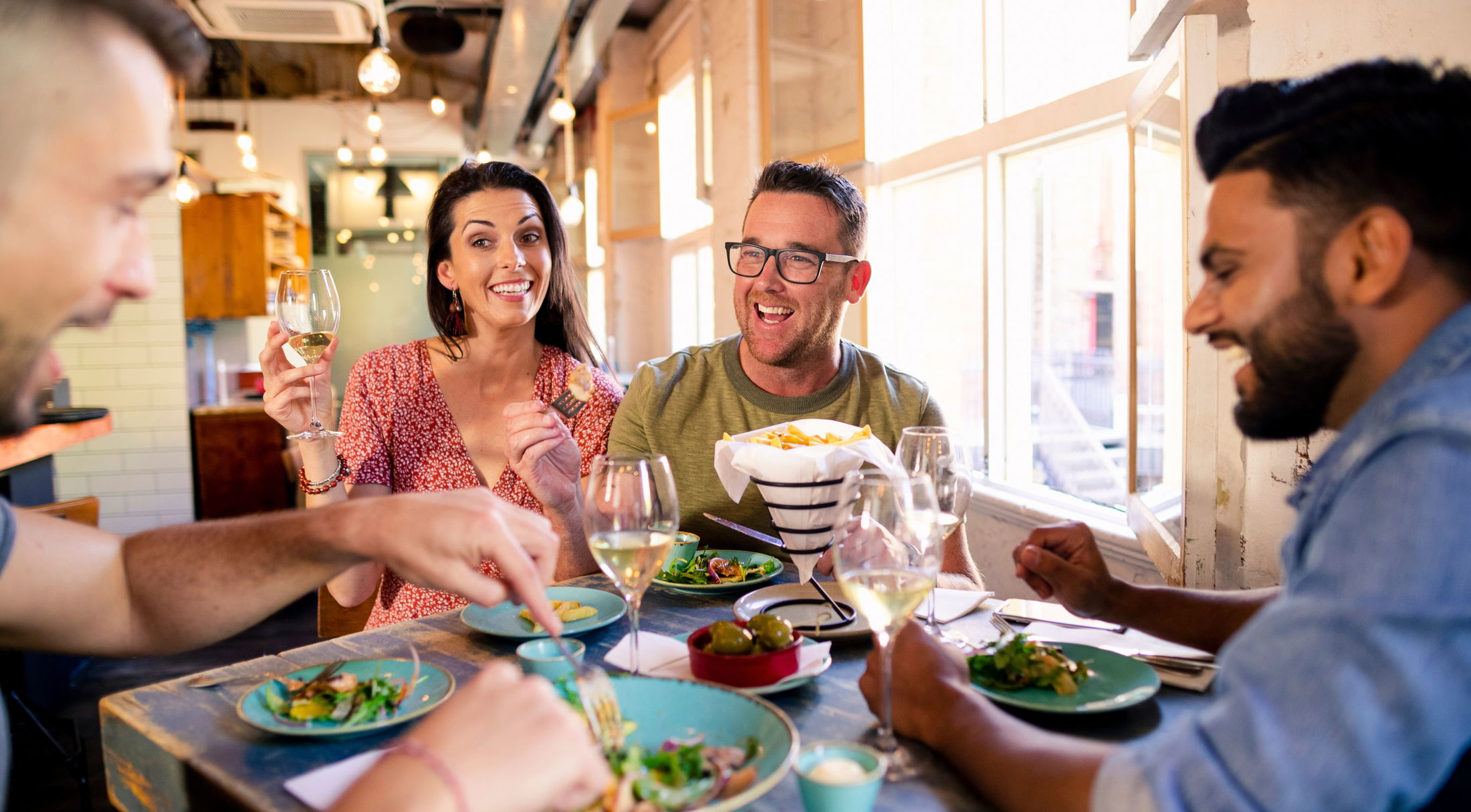 A group of friends enjoying a meal and wine together in a lively restaurant setting.