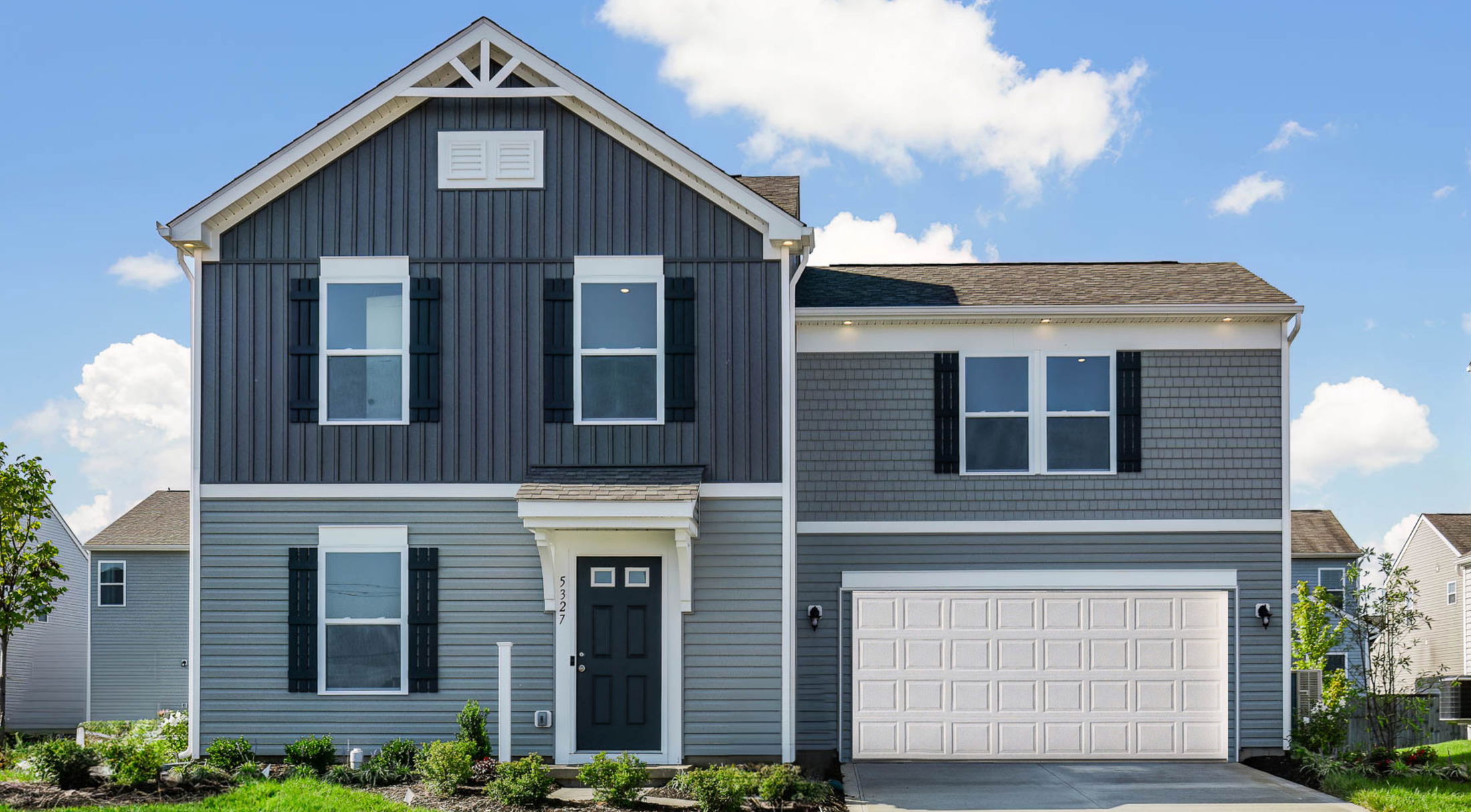 Modern two-story gray house with white trim and a double garage under a clear blue sky.