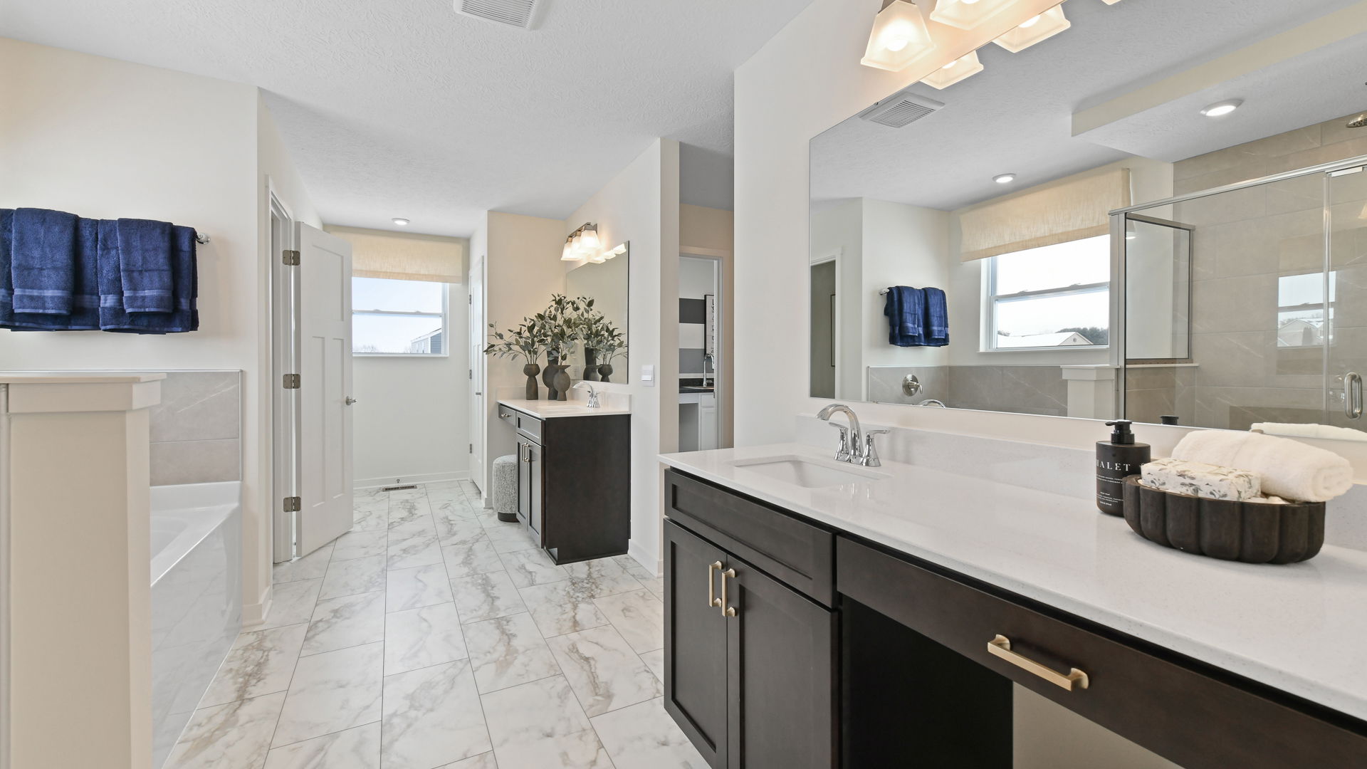 Luxurious modern bathroom with marble floors, dark wood cabinets, large mirrors, and elegant fixtures.