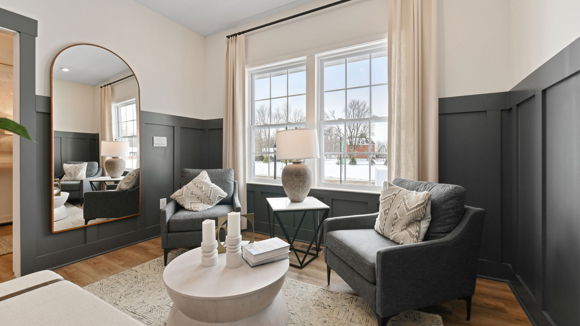 Modern living room with gray armchairs, large window, elegant lamp, and round coffee table featuring decorative candles.