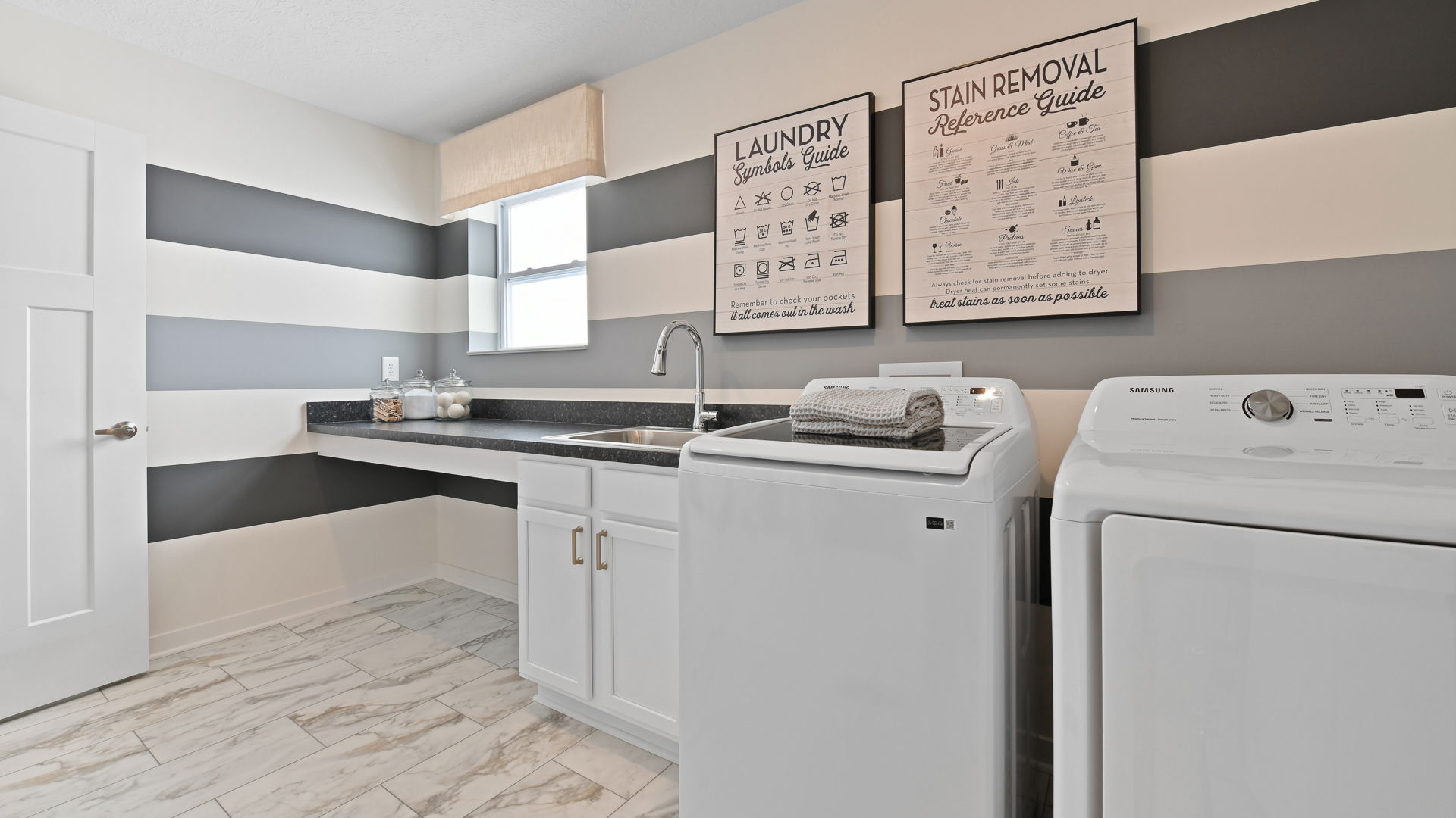 Modern laundry room with striped wall design, featuring a countertop with storage, sink, washing machine, dryer, and laundry guides on the wall.