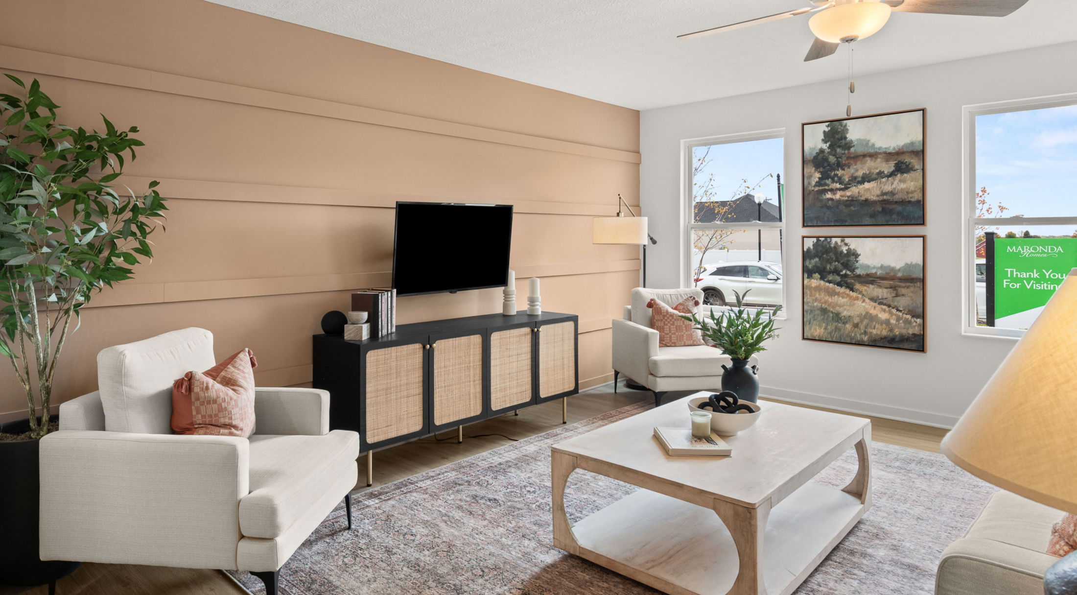 Modern living room with beige accent wall, stylish furniture, abstract art, and large windows inviting natural light.