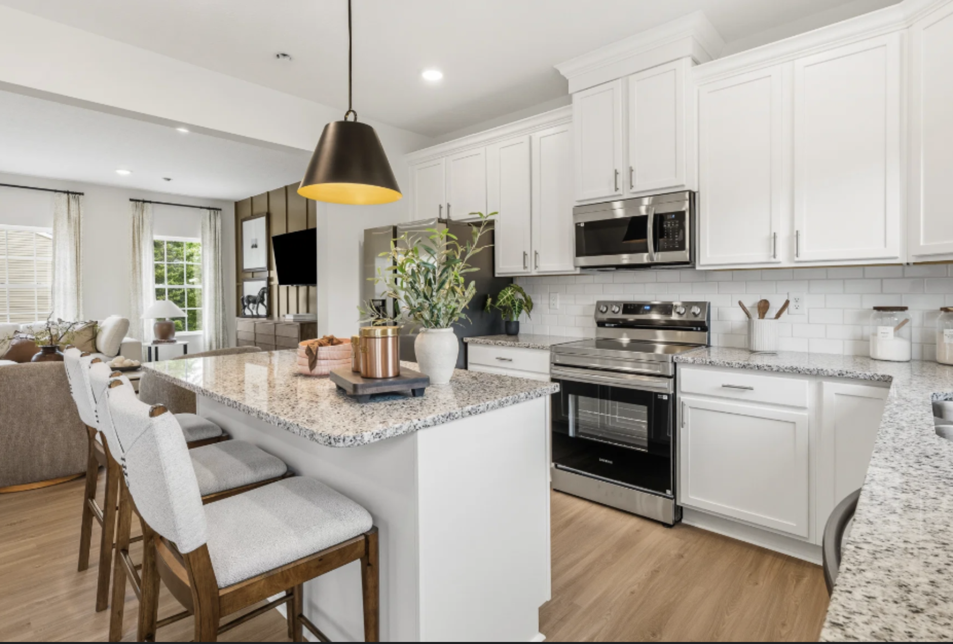 Modern kitchen featuring white cabinetry, stainless steel appliances, a granite countertop, and a dining area with bar stools.