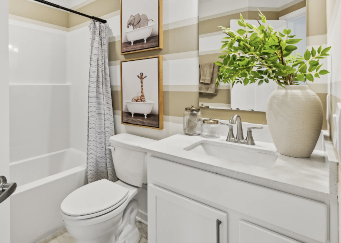 Modern bathroom featuring a bathtub with art prints, a sink with a plant in a vase, and neutral-colored walls.