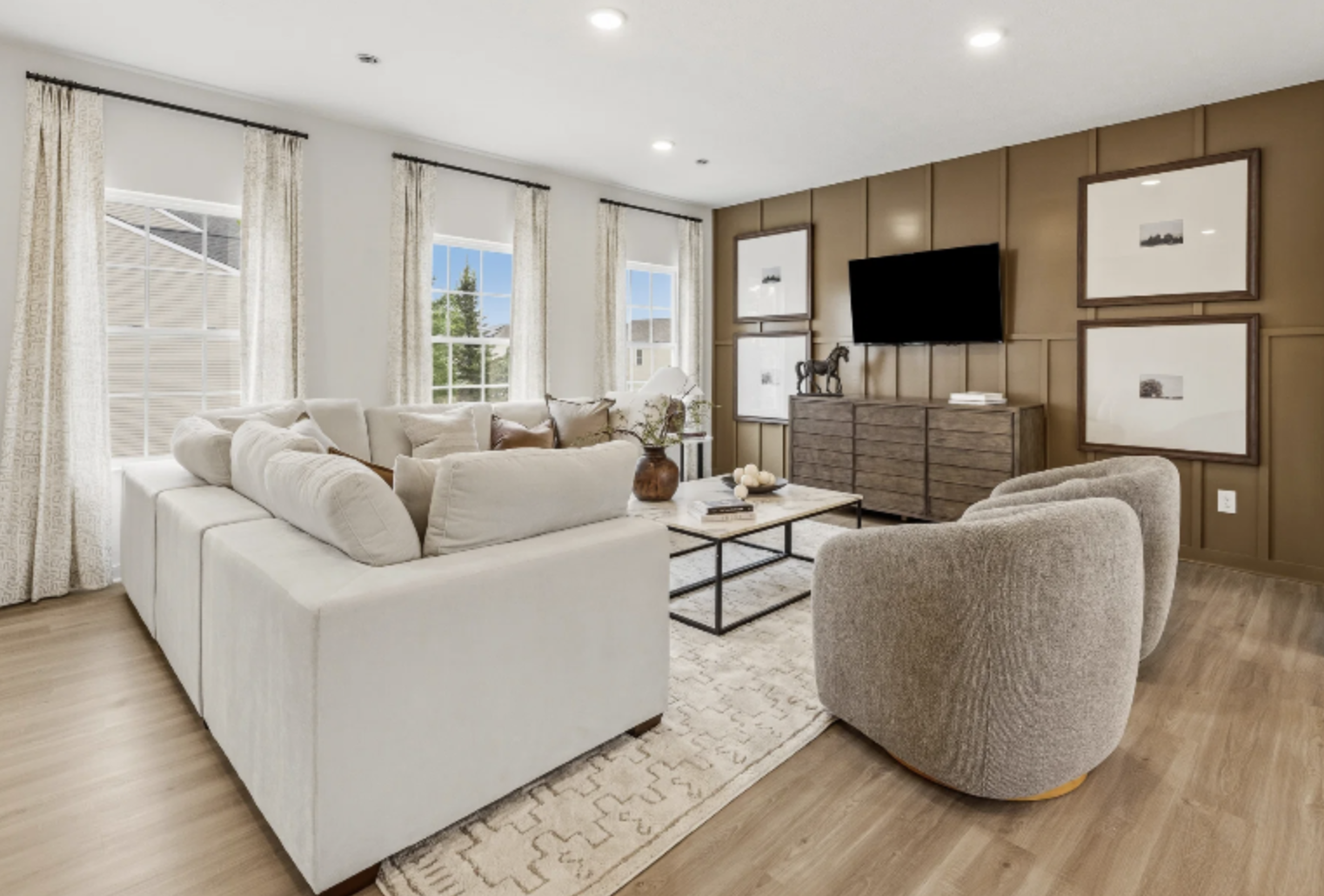 A modern living room featuring a light-colored sofa, two round armchairs, a coffee table, and decorative artwork on the walls.