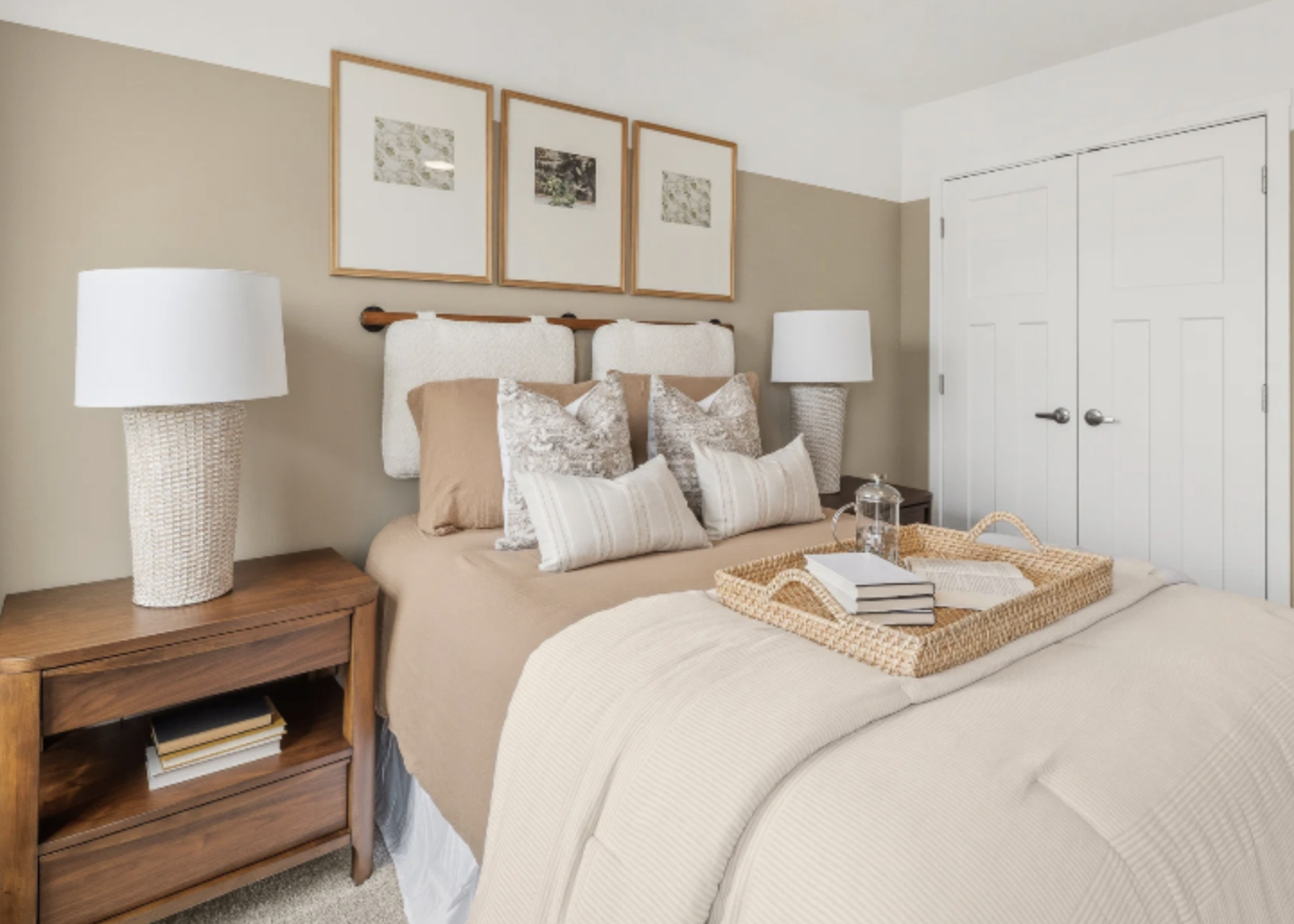 Cozy bedroom featuring a beige bedspread, decorative throw pillows, bedside tables with lamps, and framed art on the wall.