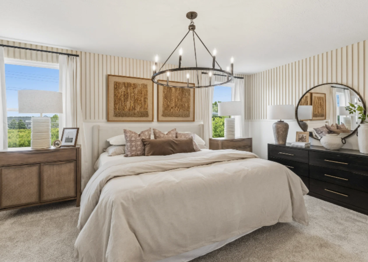 A cozy bedroom featuring a large chandelier, plush bedding, and decorative wall art with natural light streaming through the windows.