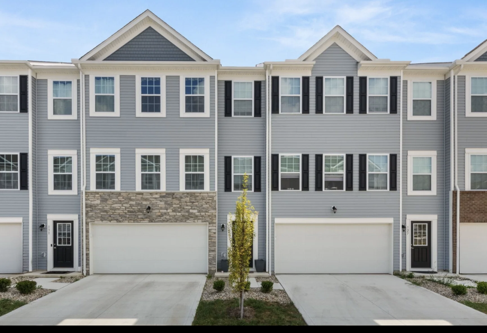 Three identical two-story townhouses with stone accents and garages, featuring large windows and a landscaped pathway.