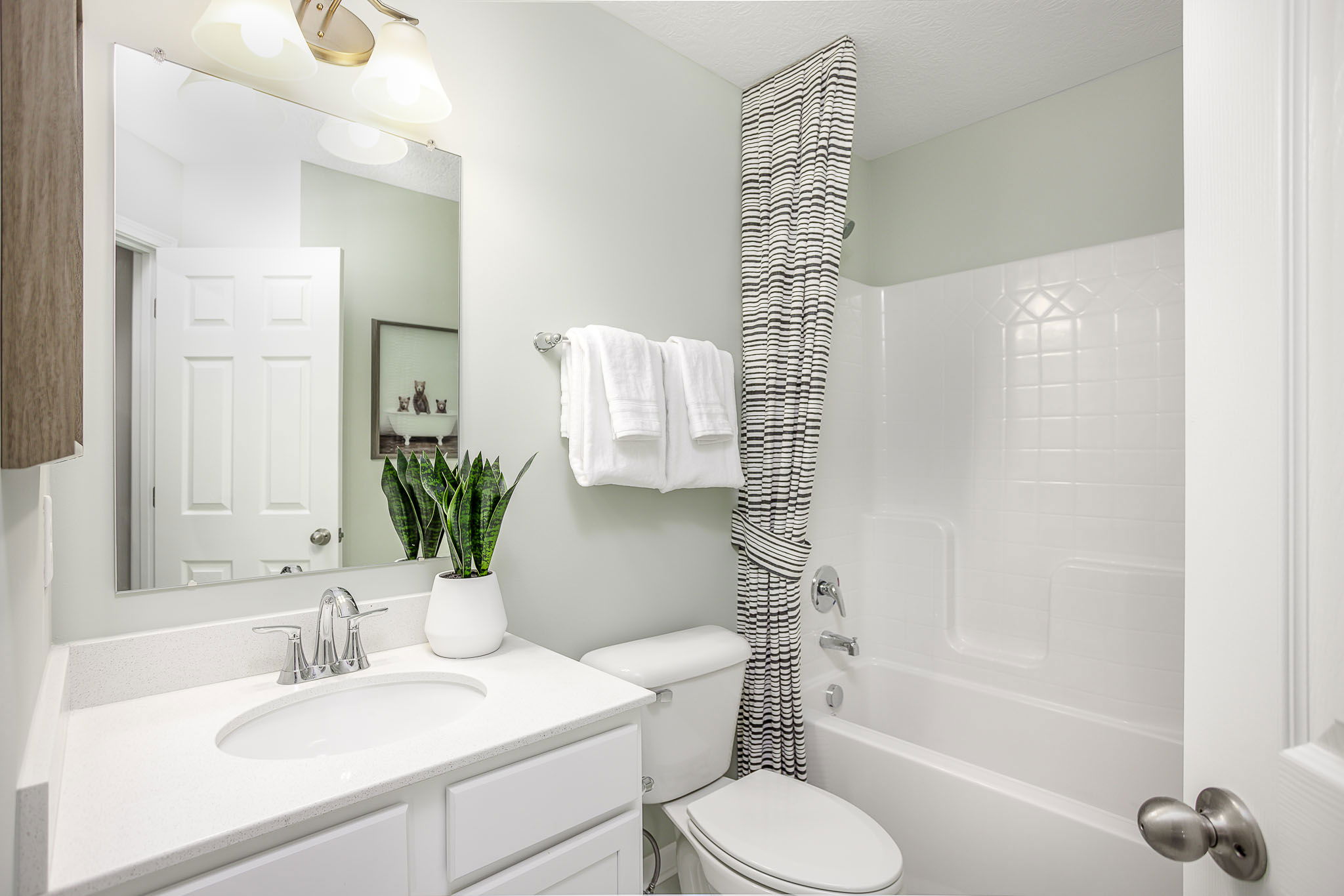 Bright, modern bathroom with white fixtures, a potted plant, striped shower curtain, and neatly folded towels.