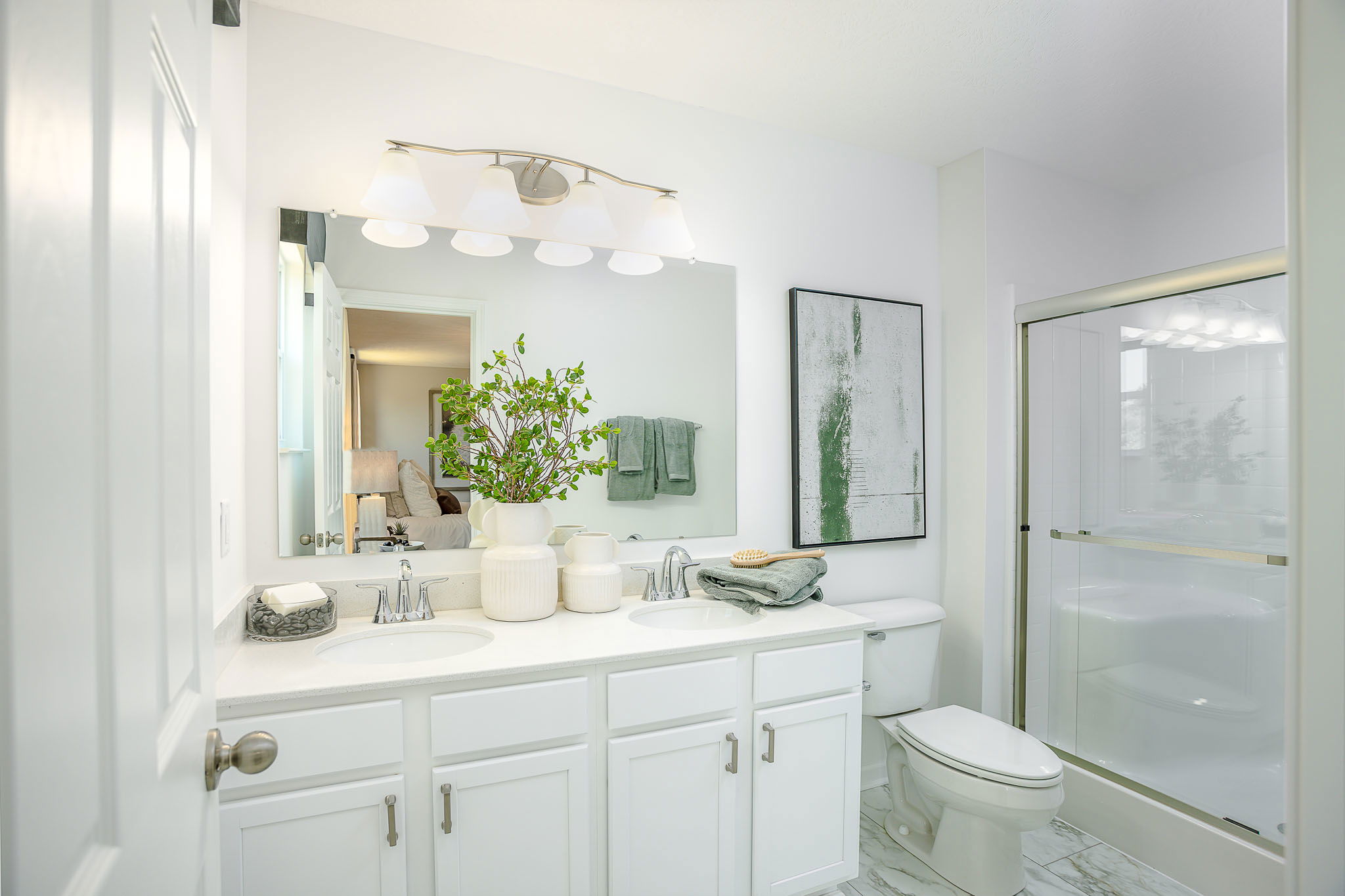 Modern white bathroom with double sink vanity, large mirror, and glass enclosed shower.