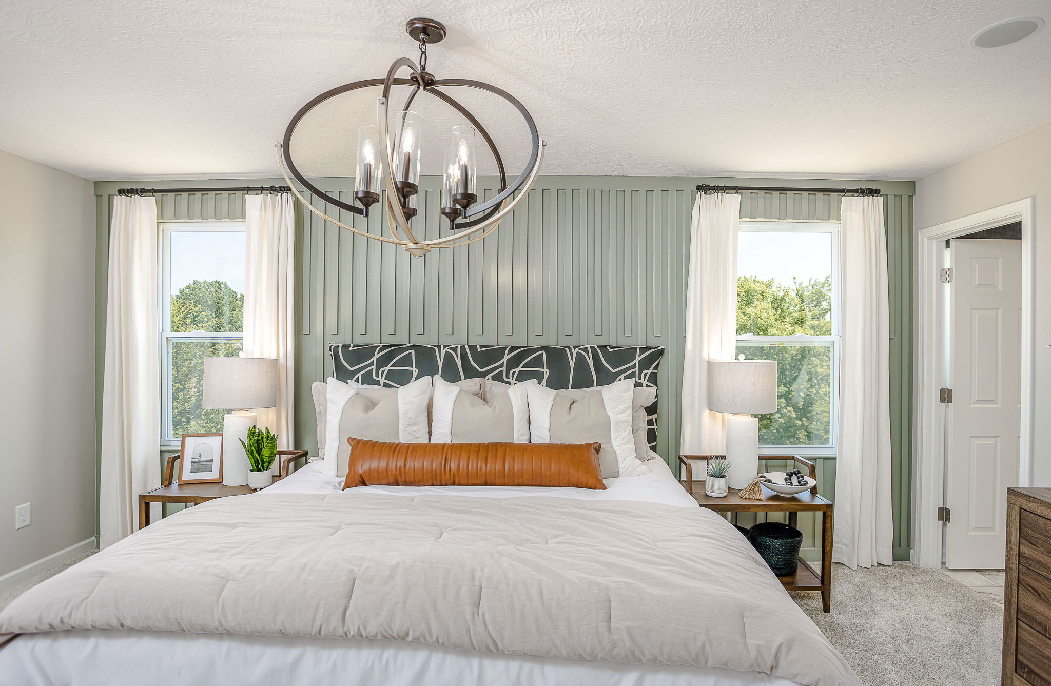 Modern bedroom featuring a plush bed with layered pillows, stylish pendant lighting, and a pastel green accent wall.