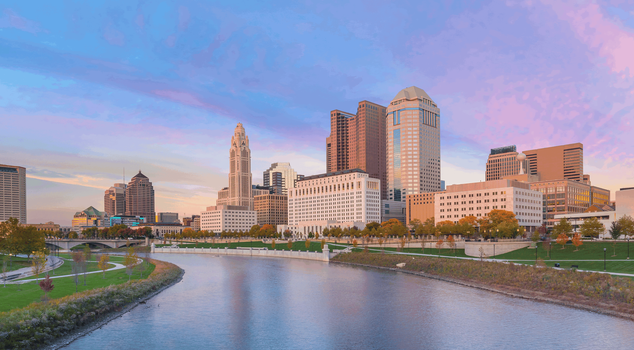 Panoramic view of the Columbus, Ohio skyline at sunset with the Scioto River in the foreground.
