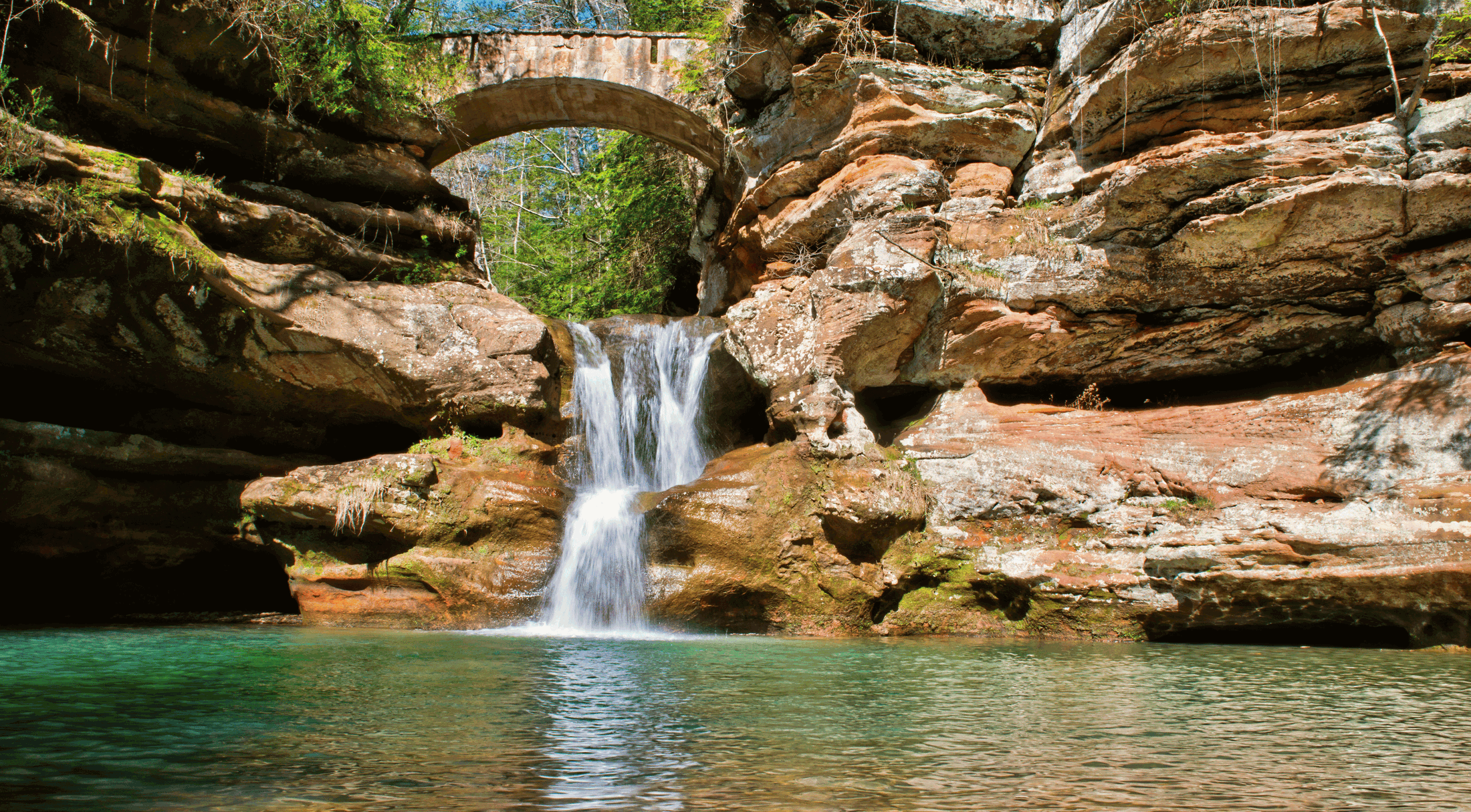 Scenic waterfall cascading under a stone bridge surrounded by rocky cliffs.