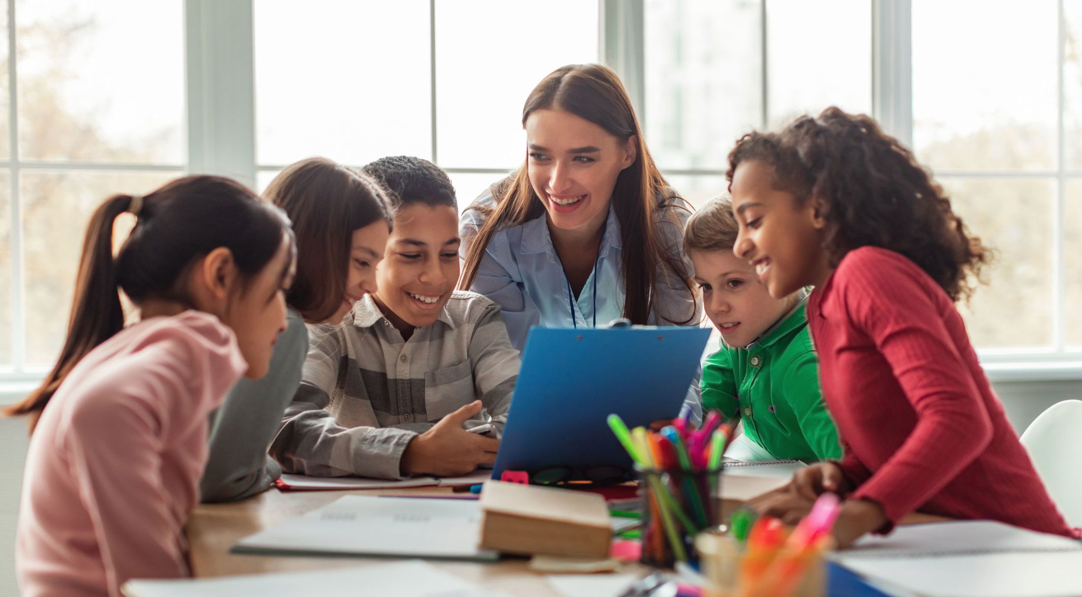 A diverse group of children enthusiastically learning with their teacher in a classroom setting.