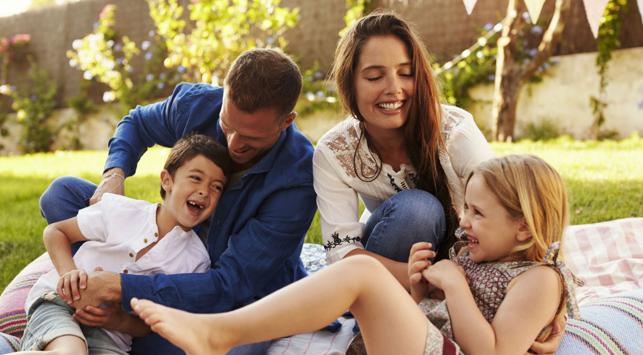 A joyful family enjoying a sunny day outdoors on a picnic blanket, laughing and playing together in a garden.
