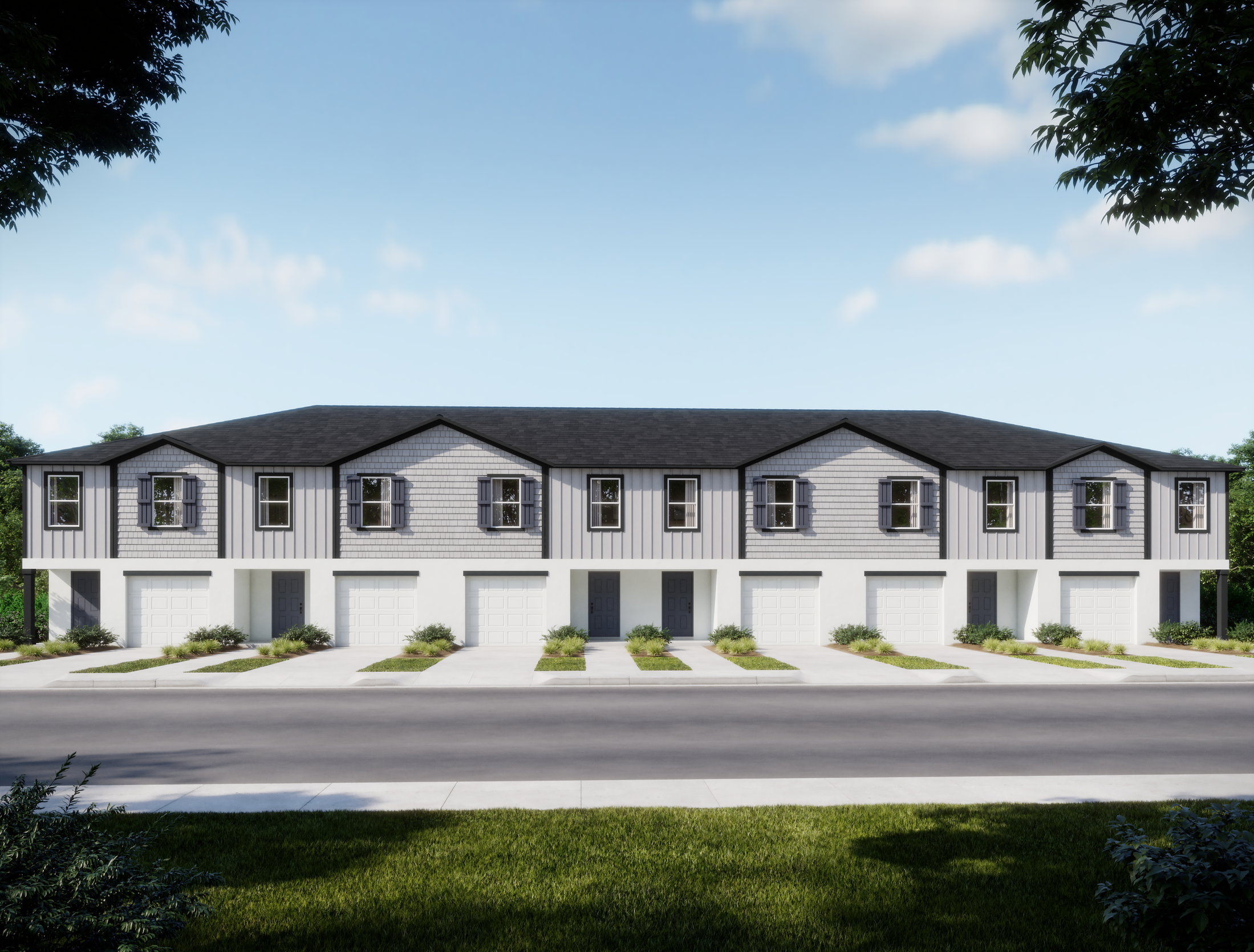 A row of modern townhouses with a manicured lawn and driveway under a clear blue sky.