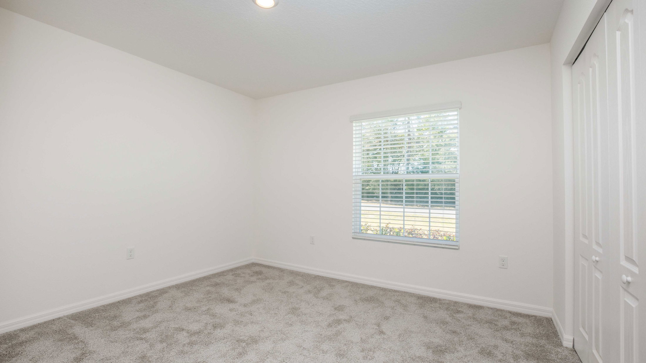 Empty room with white walls, carpeted floor, and a window with blinds letting in natural light.