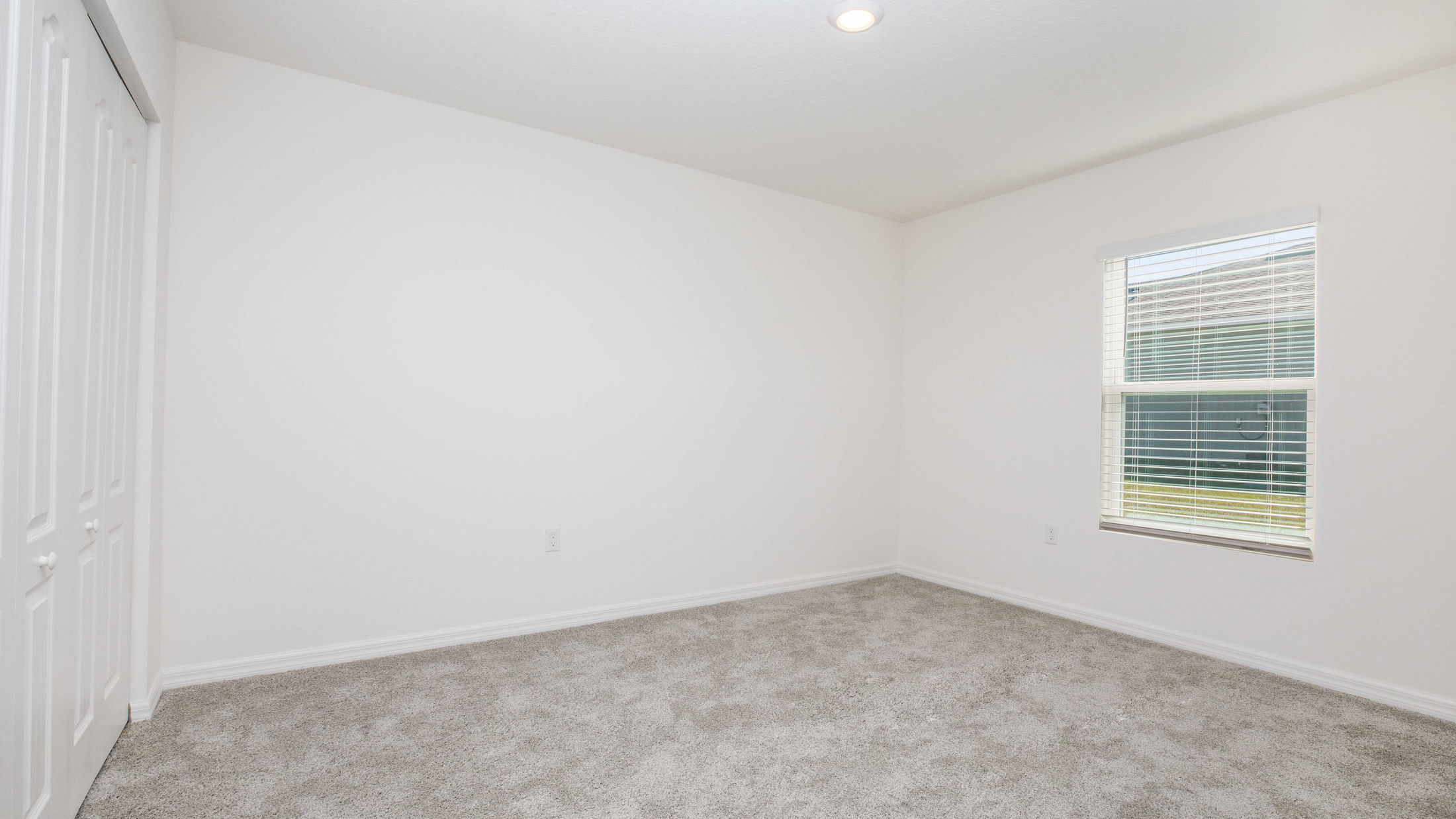 Empty room with white walls, carpet flooring, a window with blinds, and a closed wardrobe.