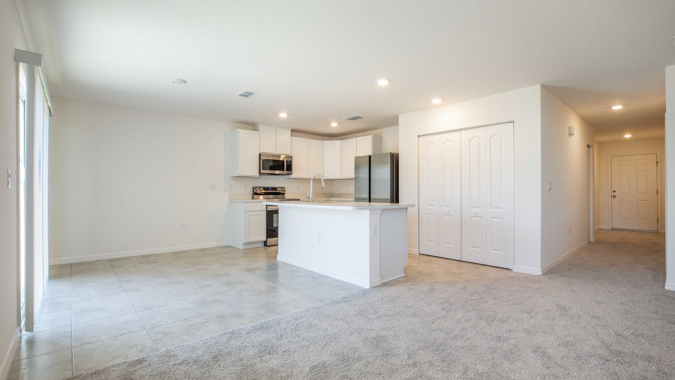 Modern open-concept kitchen and living area featuring white cabinets, stainless steel appliances, and sleek tile flooring.