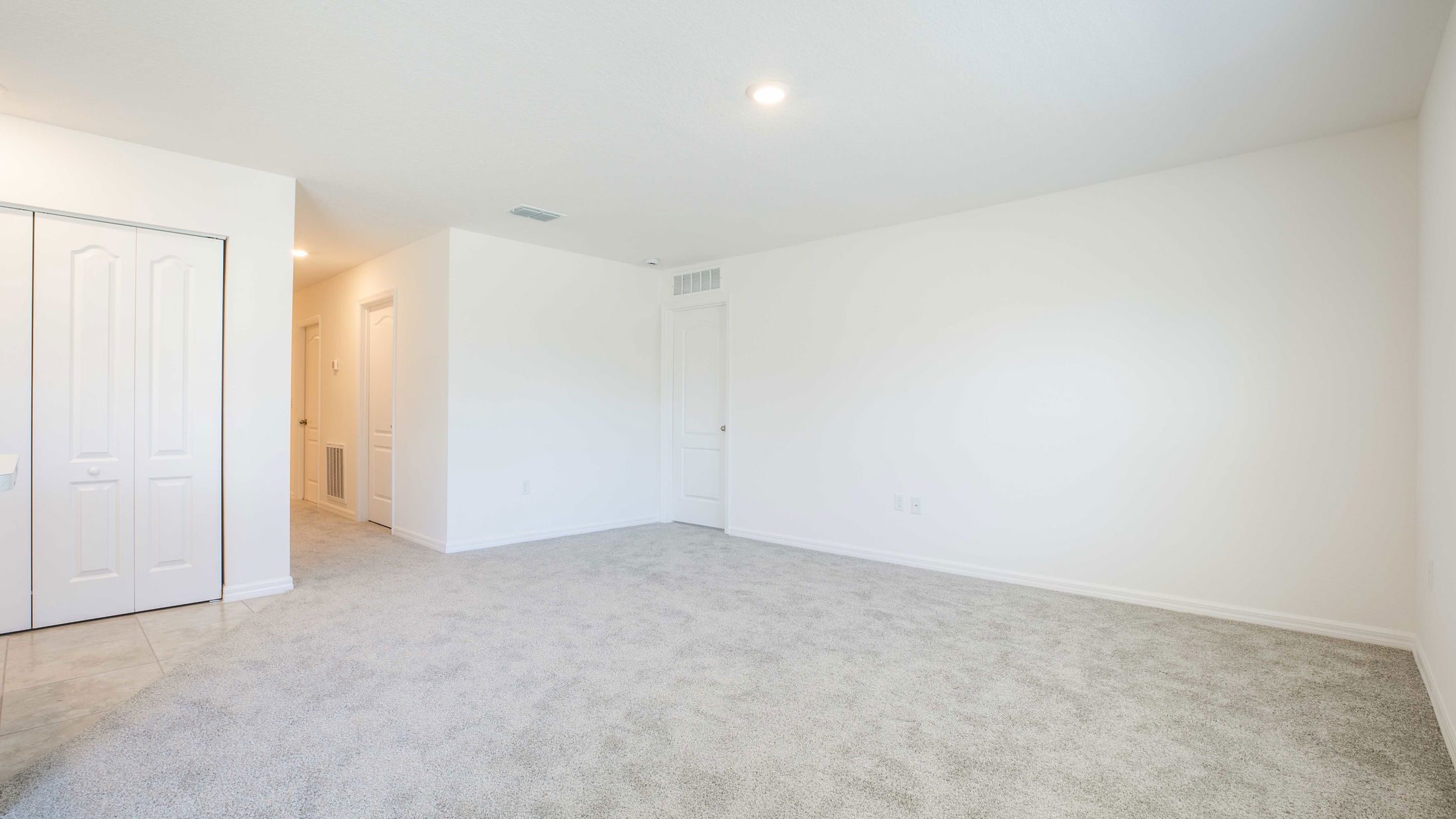 Empty room with white walls, beige carpet, and a closed closet door, offering ample space and natural lighting.