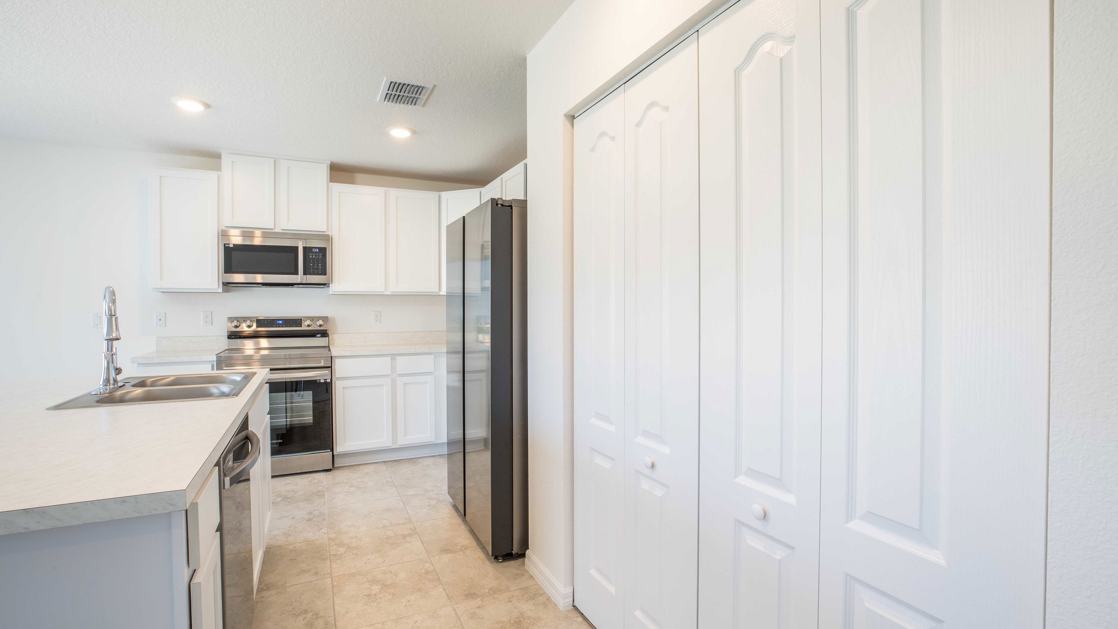 Modern kitchen featuring white cabinets, stainless steel appliances, and a sleek sink under recessed lighting.