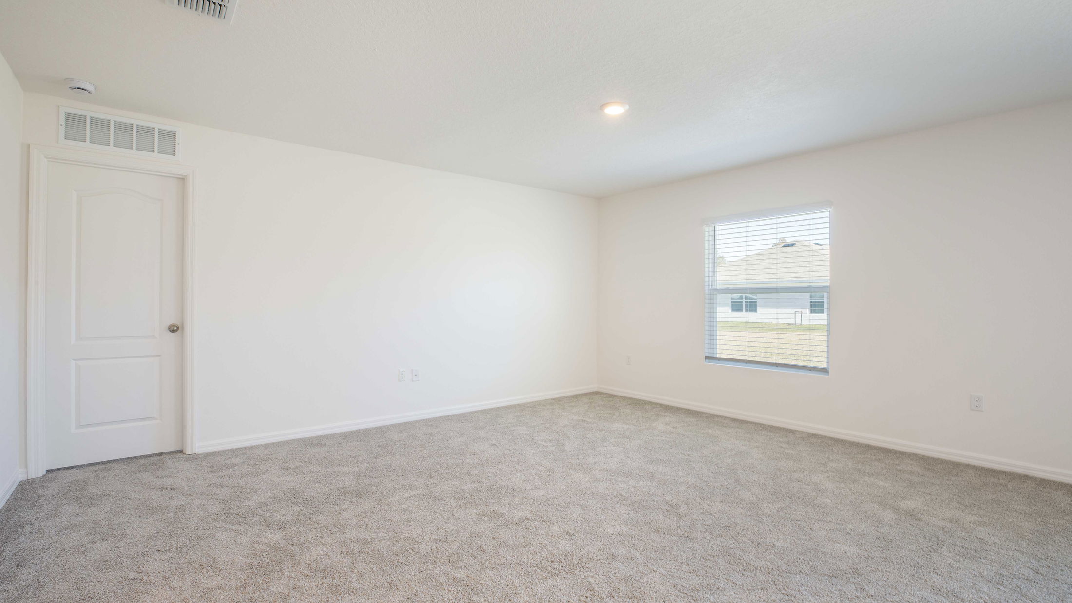 Empty white-walled room with plush gray carpet and natural light through a window.
