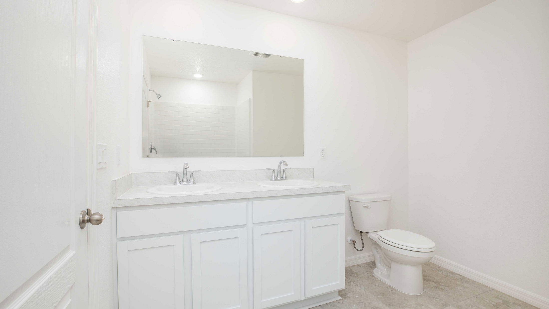 Modern white bathroom with dual sinks, large mirror, and toilet on tiled floor.