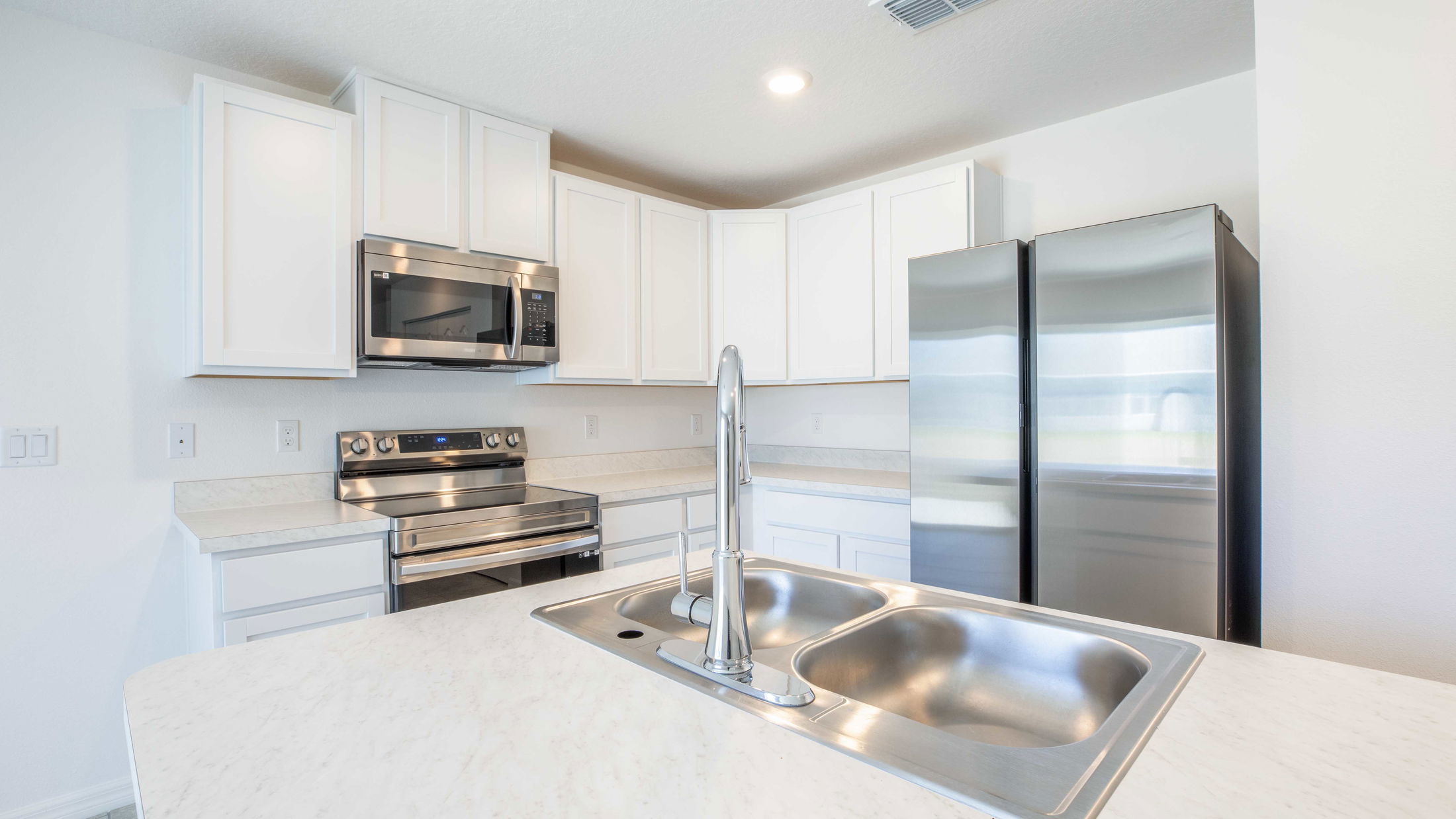 Modern kitchen with white cabinets, stainless steel appliances, and a double sink on a marble countertop.